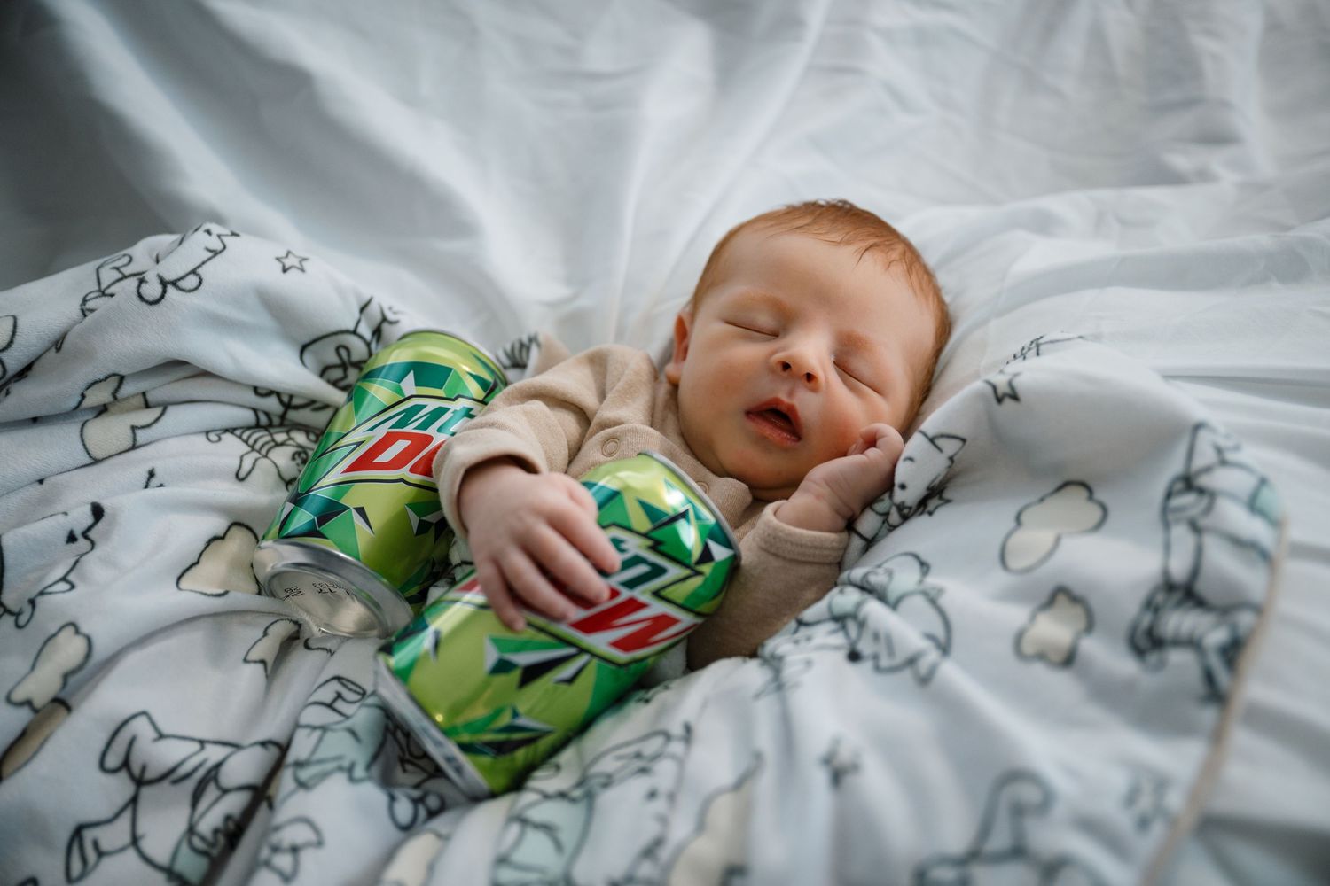 Sleeping baby in green patterned clothing rests on white bedding with cartoon prints.