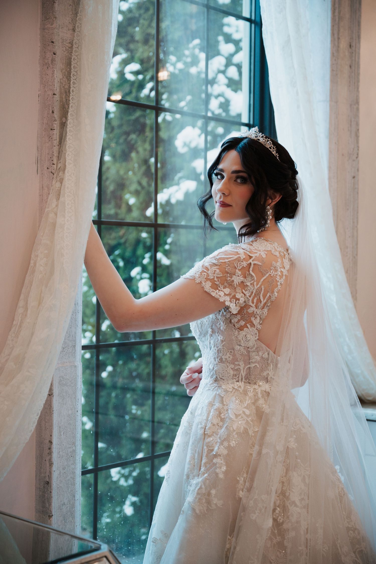 Ethereal bridal portrait by a window with lace dress and veil.