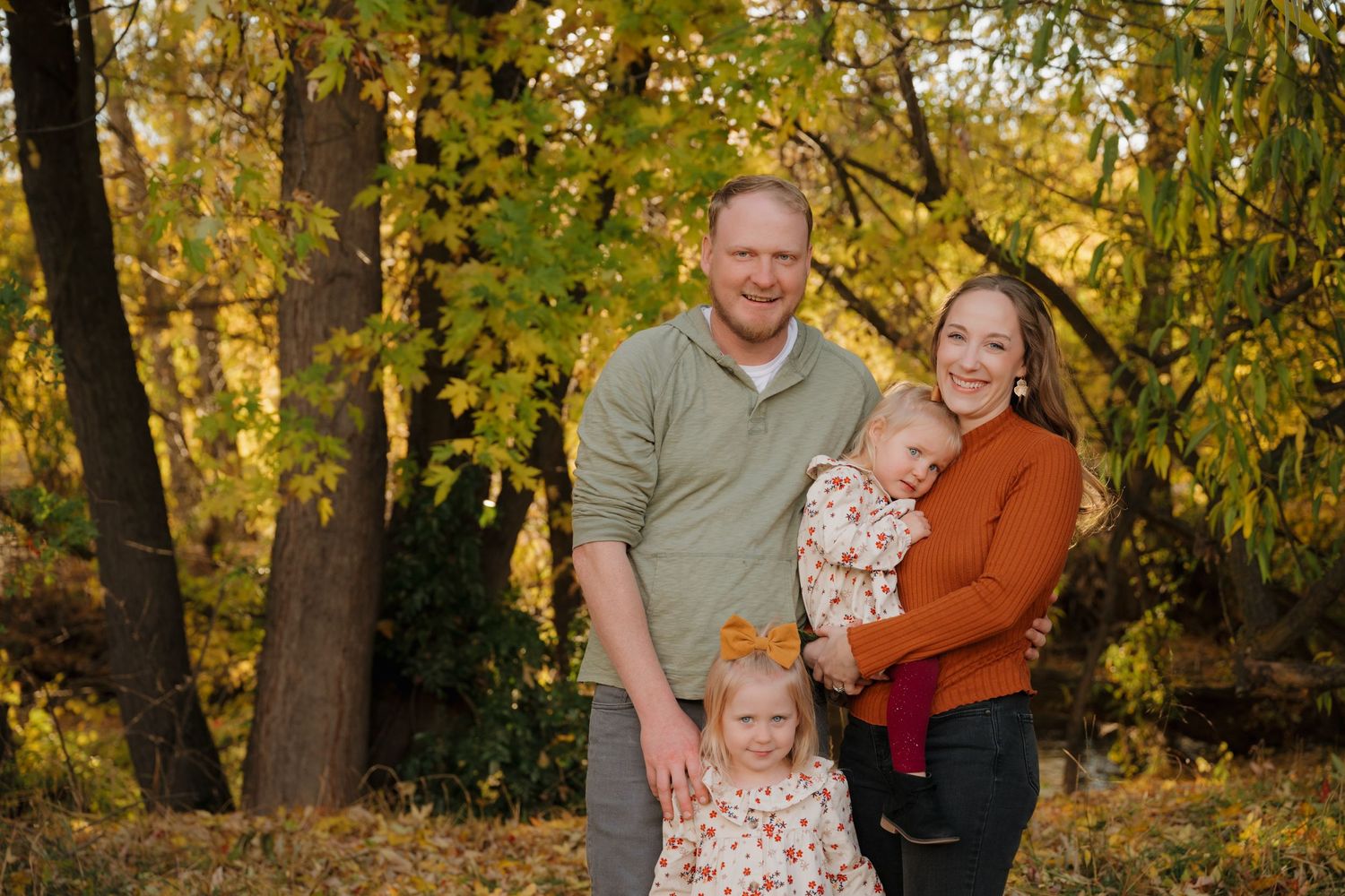 Autumn family portrait with coordinated rust and neutral colored outfits among fall foliage.