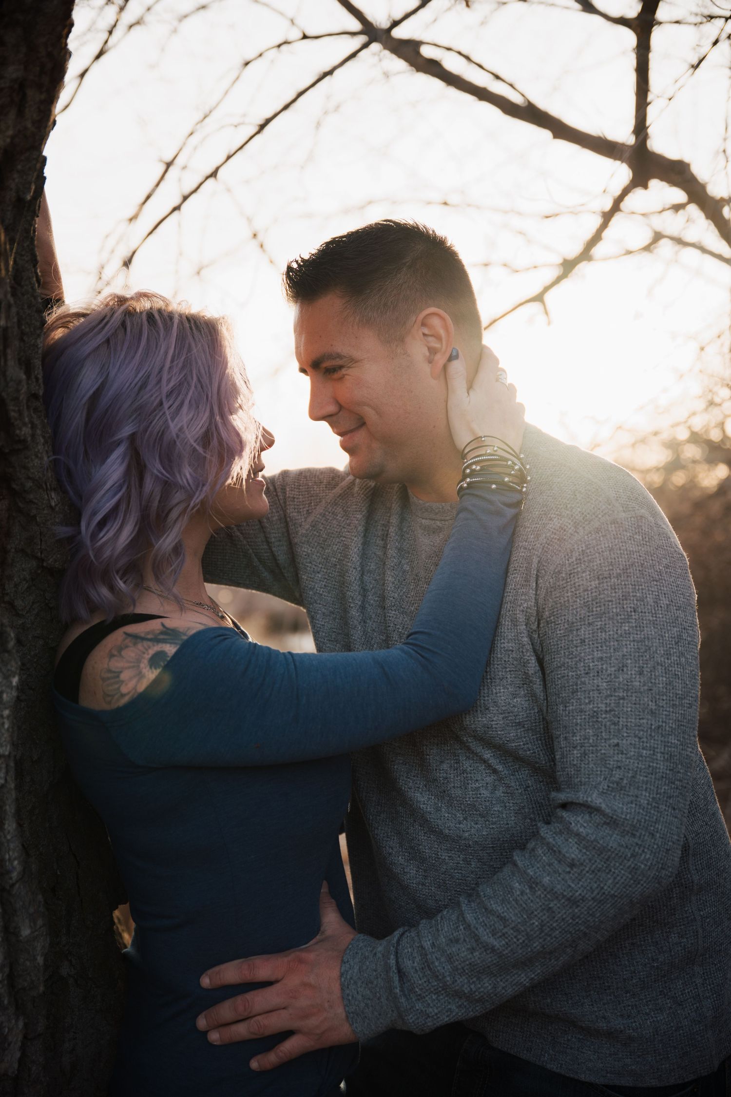 Intimate backlit portrait of couple embracing against bare winter trees.