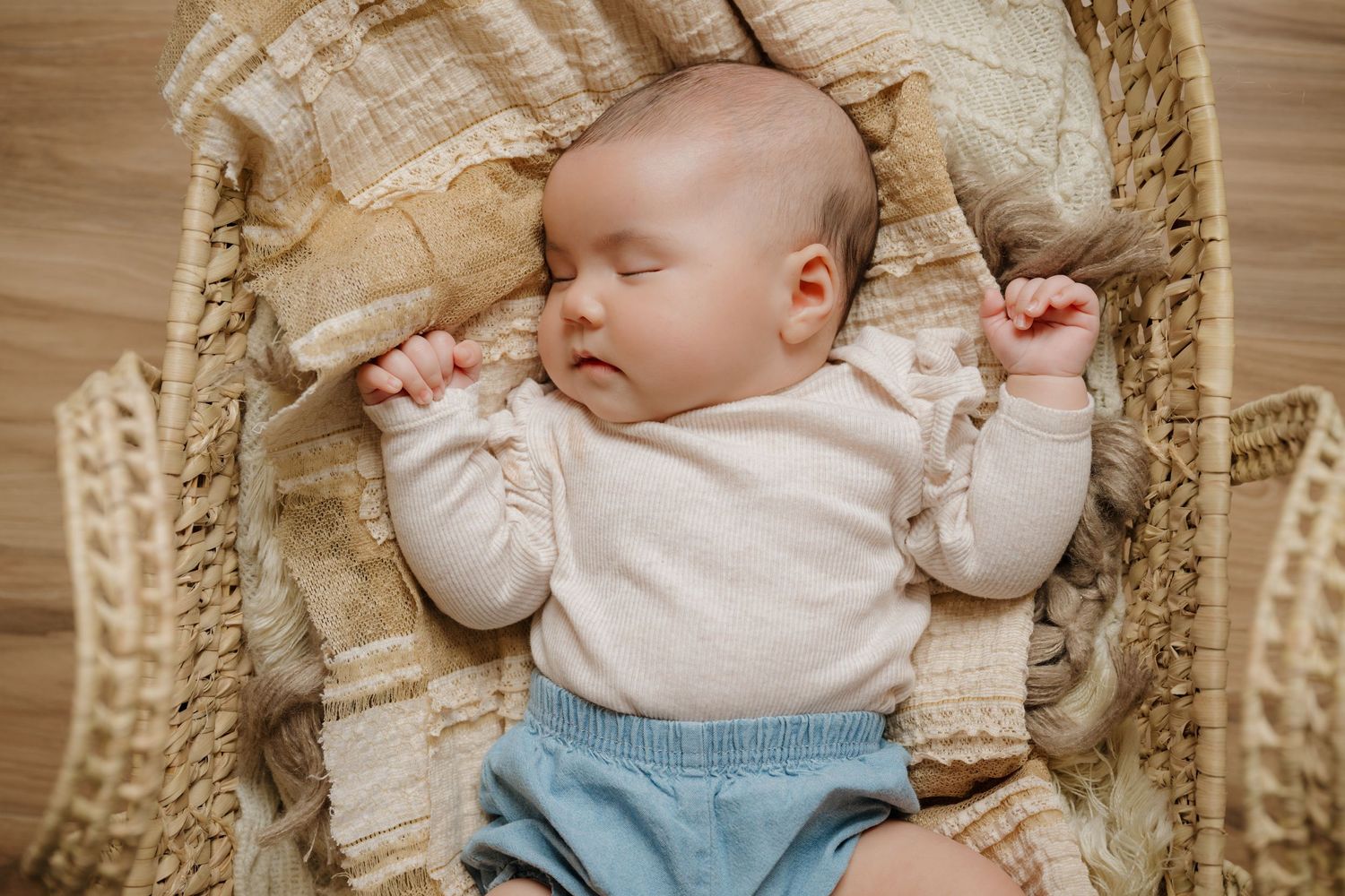 Nampa, Idaho Newborn Photographer. Peaceful sleeping baby in a cream-colored knit outfit resting in a woven bassinet.