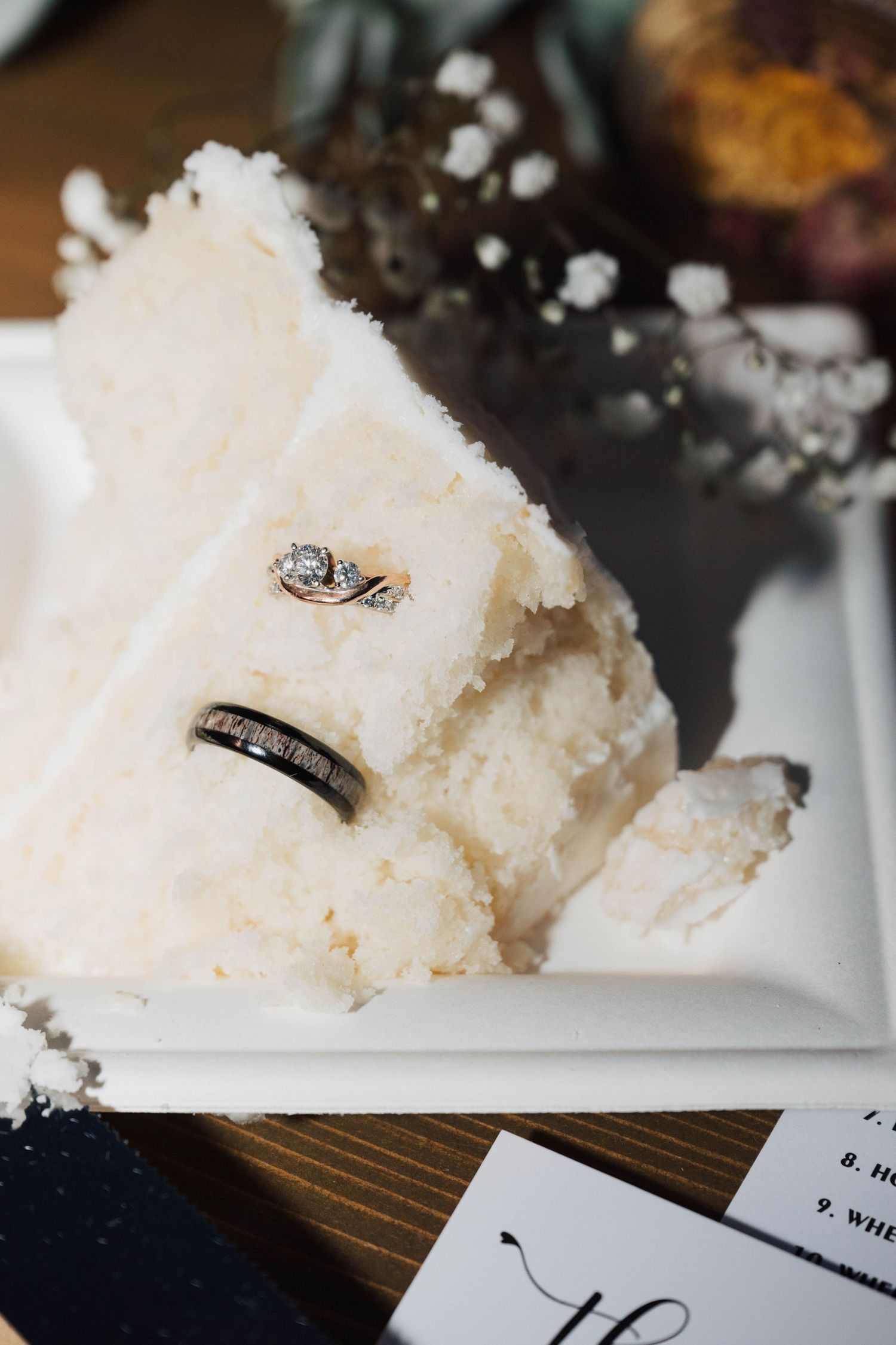 Wedding rings nestled in the layers of a white wedding cake, creating an artistic detail shot.