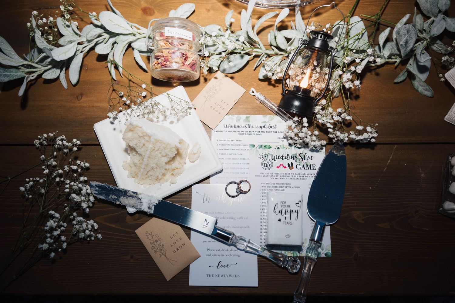 Wedding invitations and rings lay on wooden table surrounded by delicate white flowers and invitation envelopes.