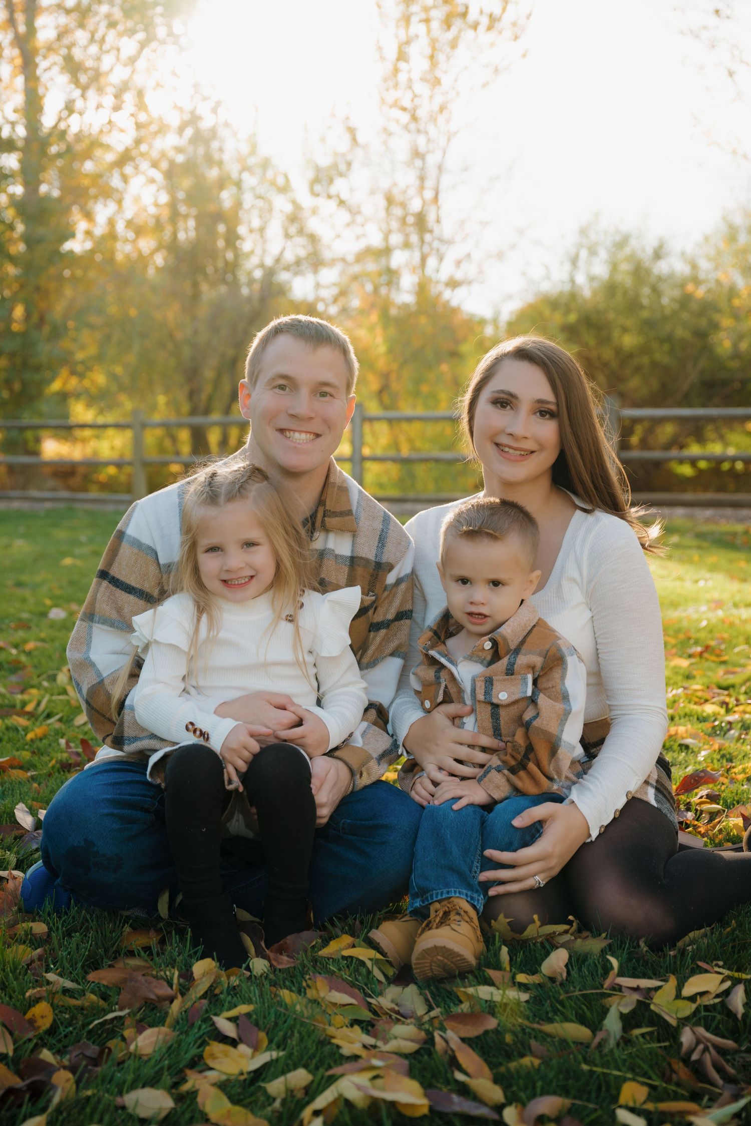 Happy family sitting on grass during golden hour autumn photoshoot with coordinated outfits.