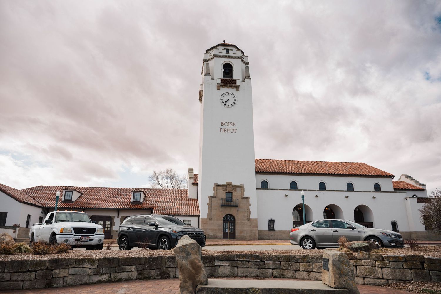 A white Spanish colonial style train station with a prominent clock tower stands under moody clouds in Boise, Idaho.