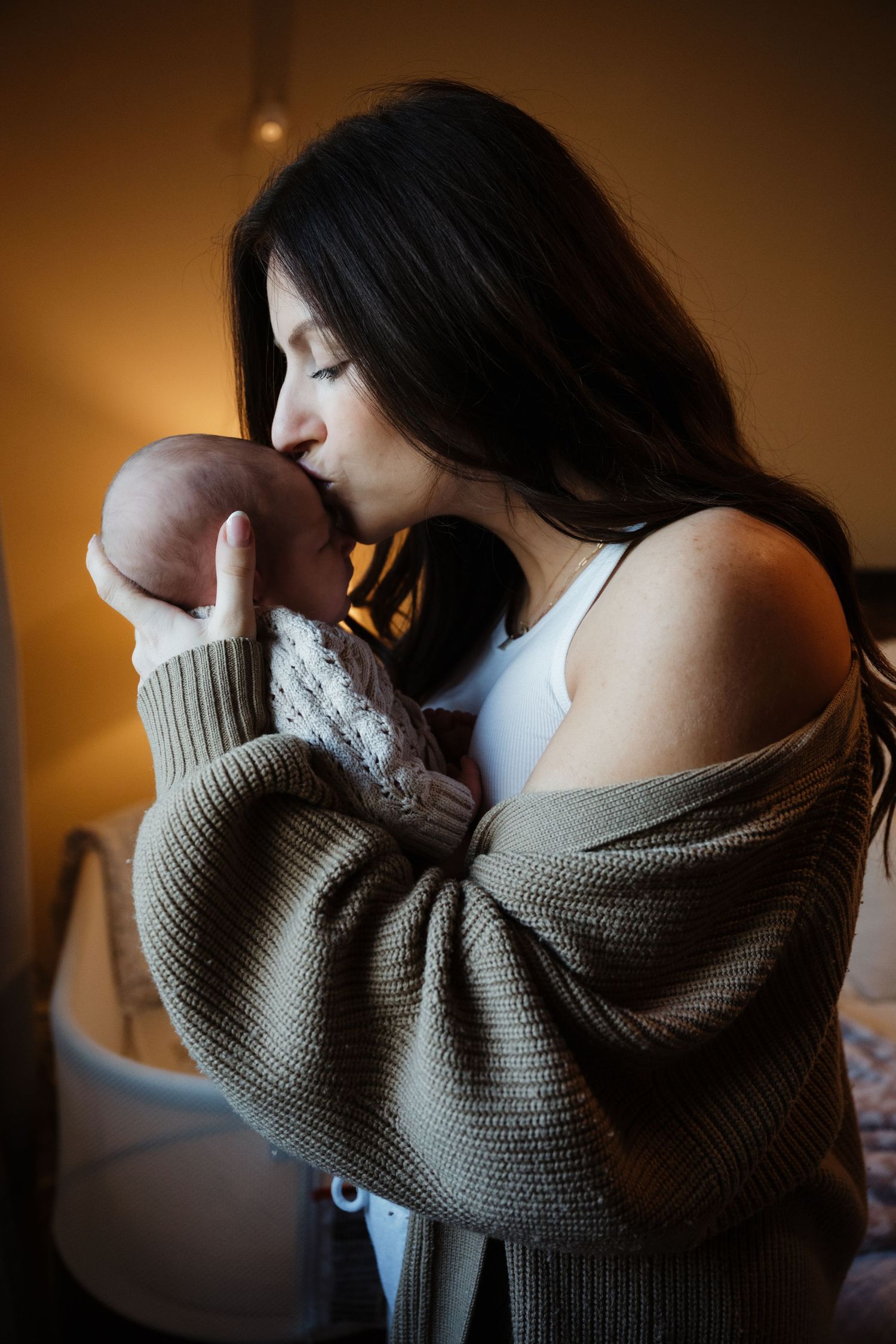 Intimate moment with a baby wrapped in knit clothing against warm lighting.