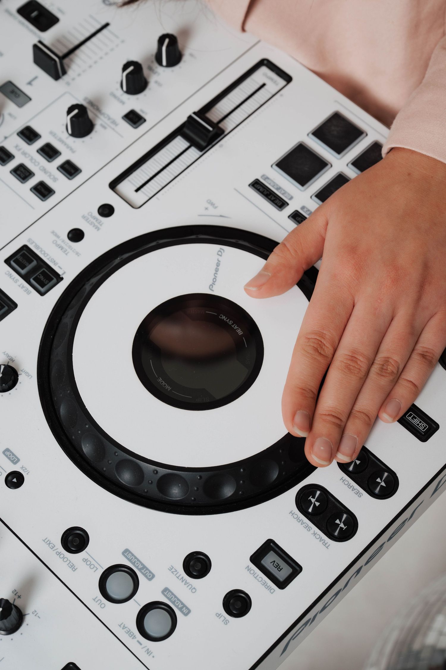 Hand adjusting controls on a white professional DJ controller with knobs, buttons and a large circular jog wheel.