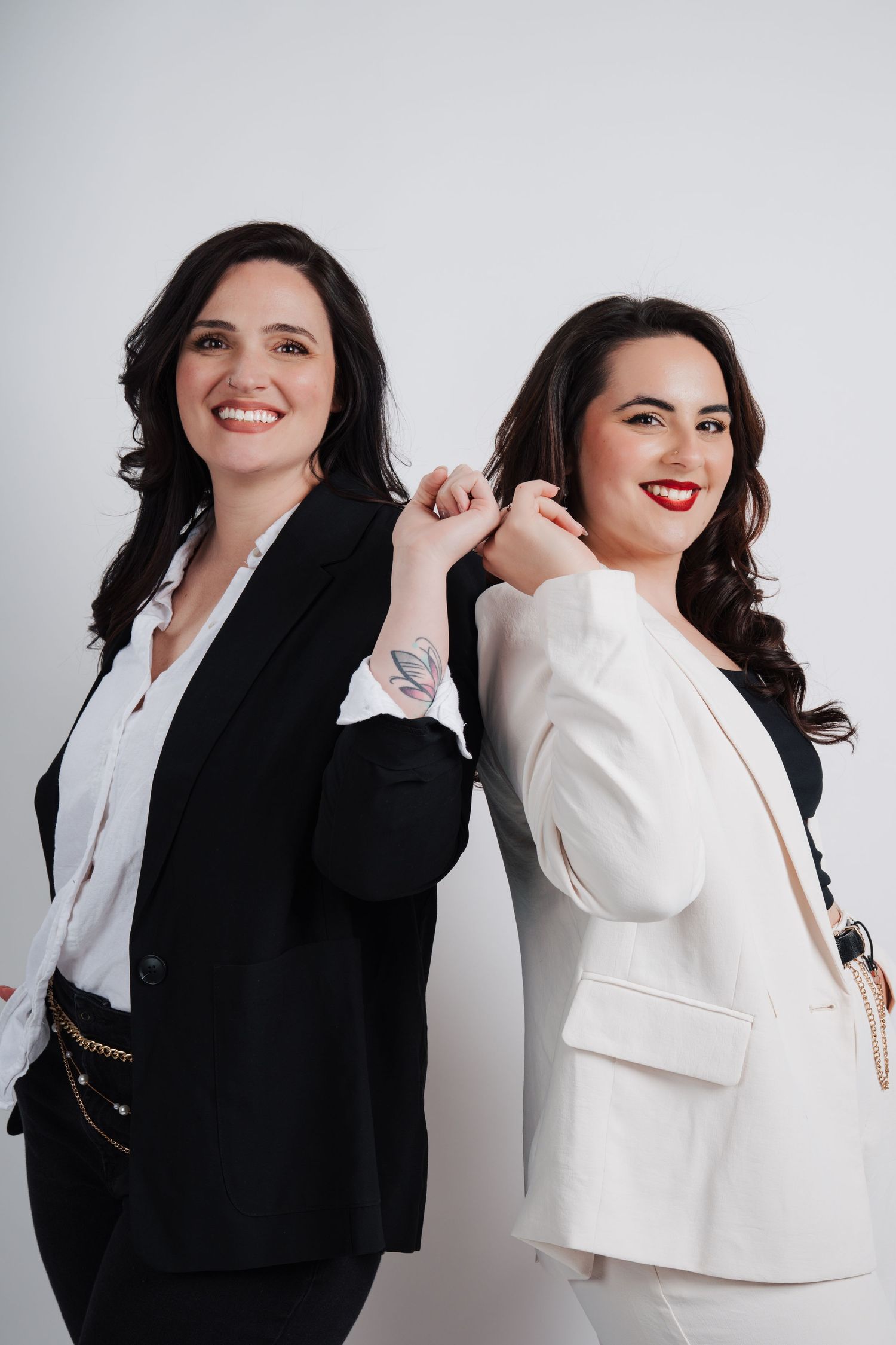 Two women in contrasting black and white blazers pose back-to-back against a light background.