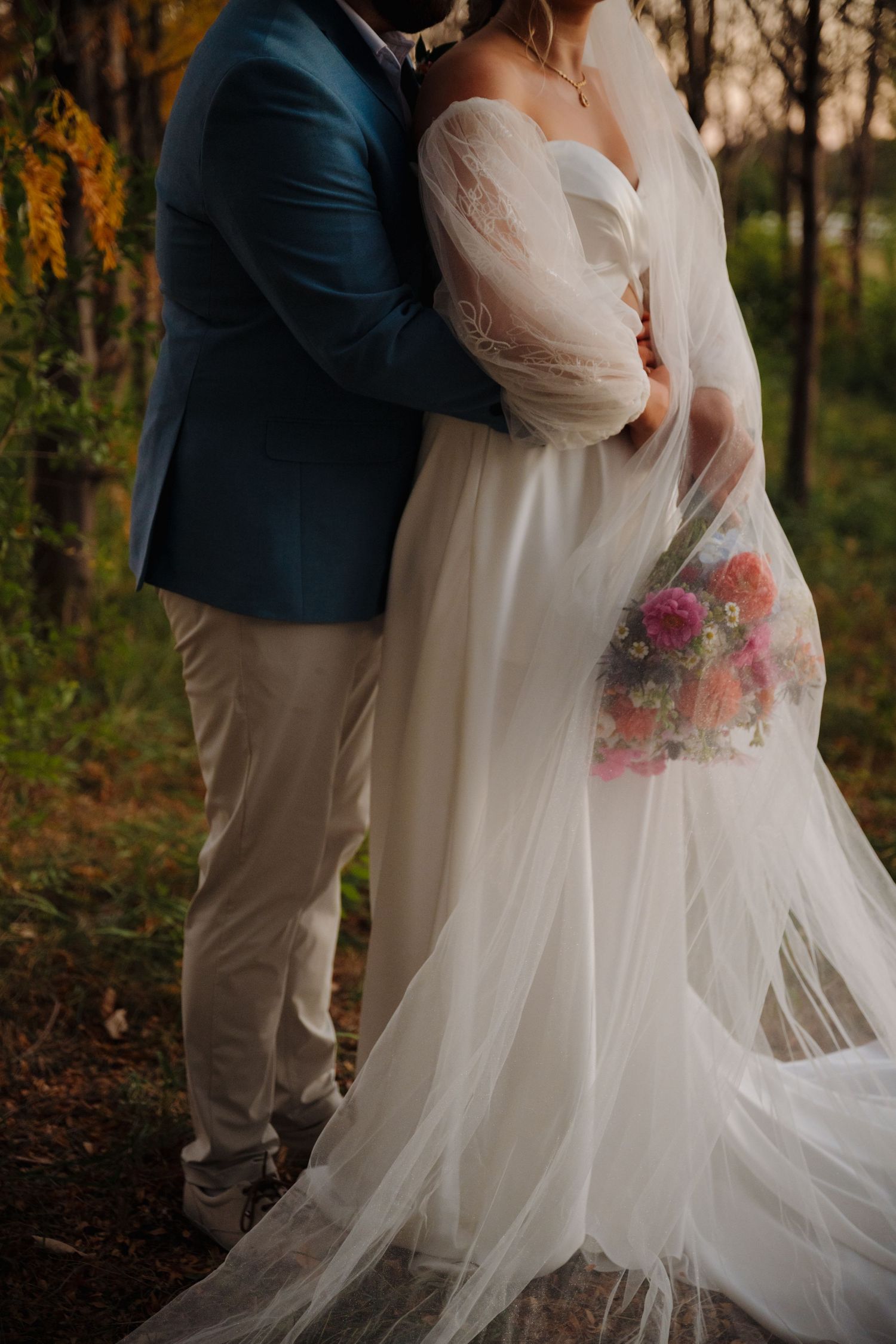 Close-up of a couple in wedding attire with focus on the bride's flowing dress and colorful bouquet.