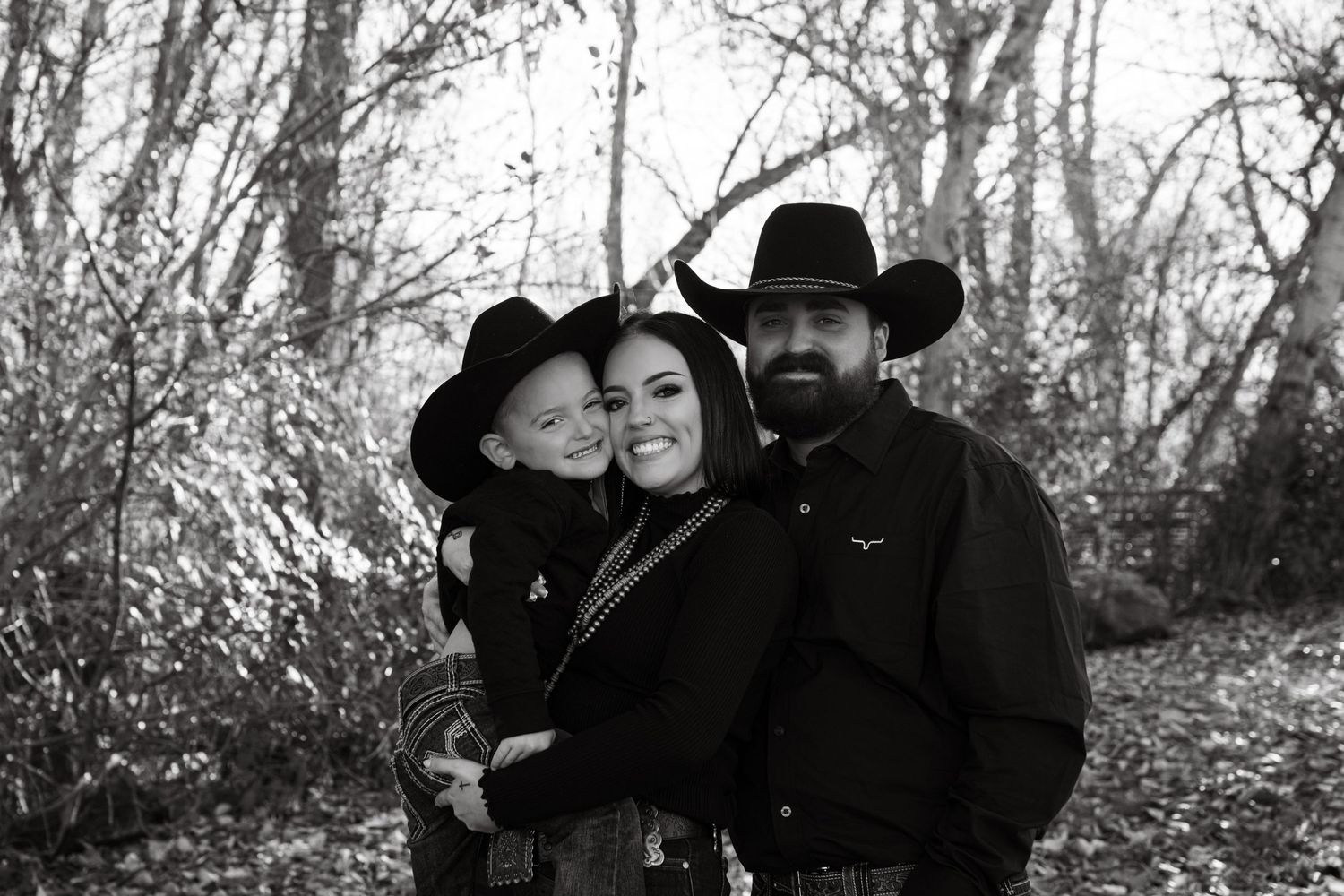 Black and white family portrait in western attire outdoors with fall foliage backdrop.