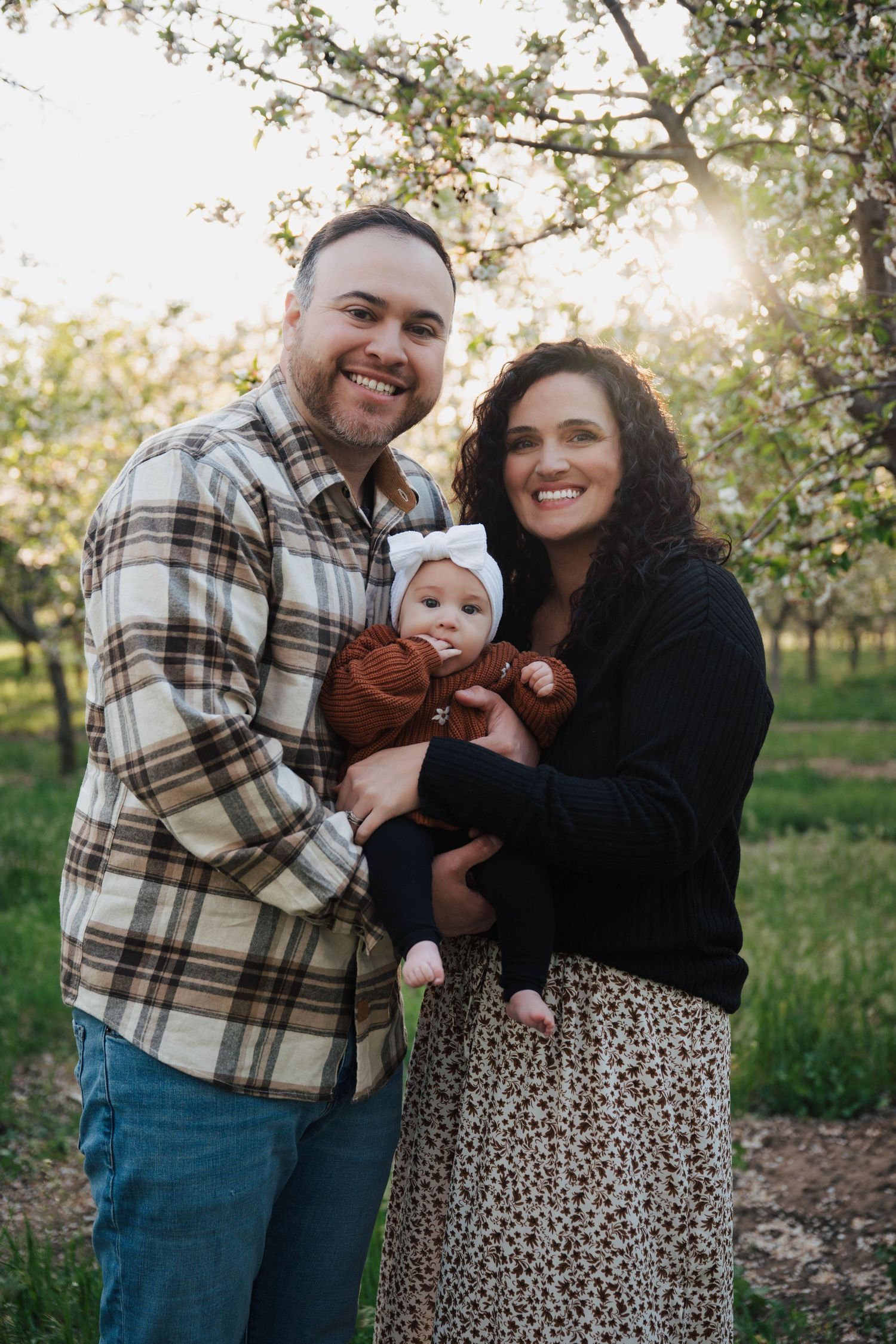 Family portrait taken outdoors in an orchard at sunset with warm lighting and autumn scenery.