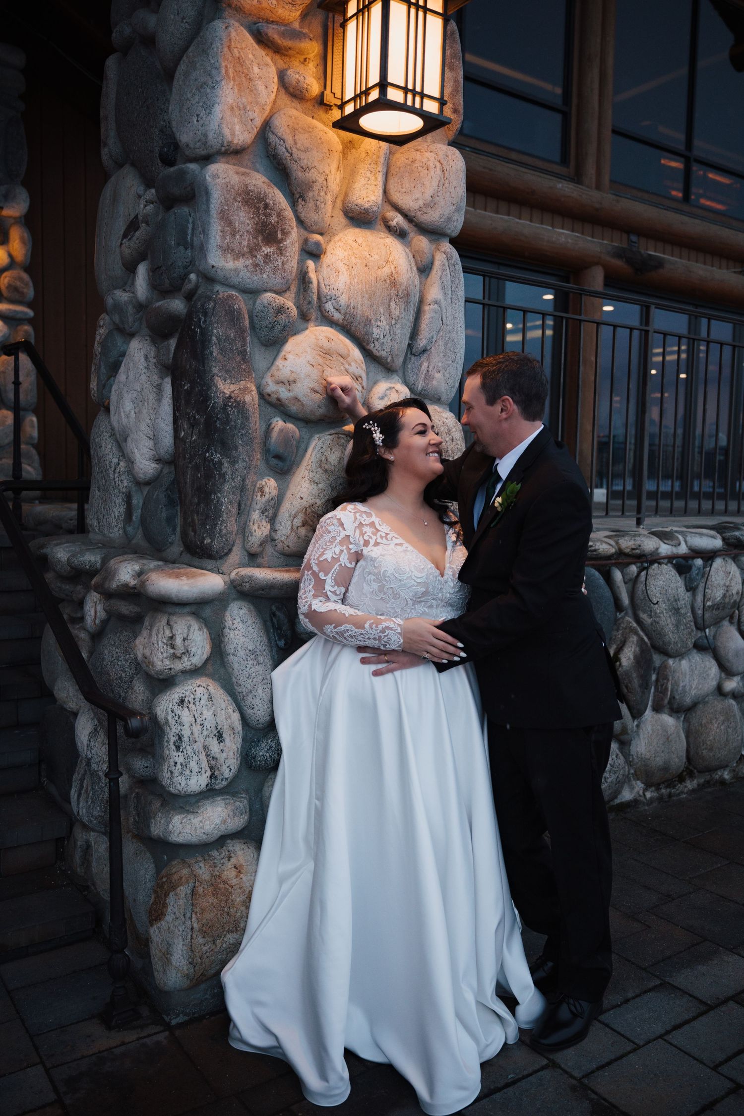 Wedding couple sharing an intimate moment against a stone pillar at dusk.