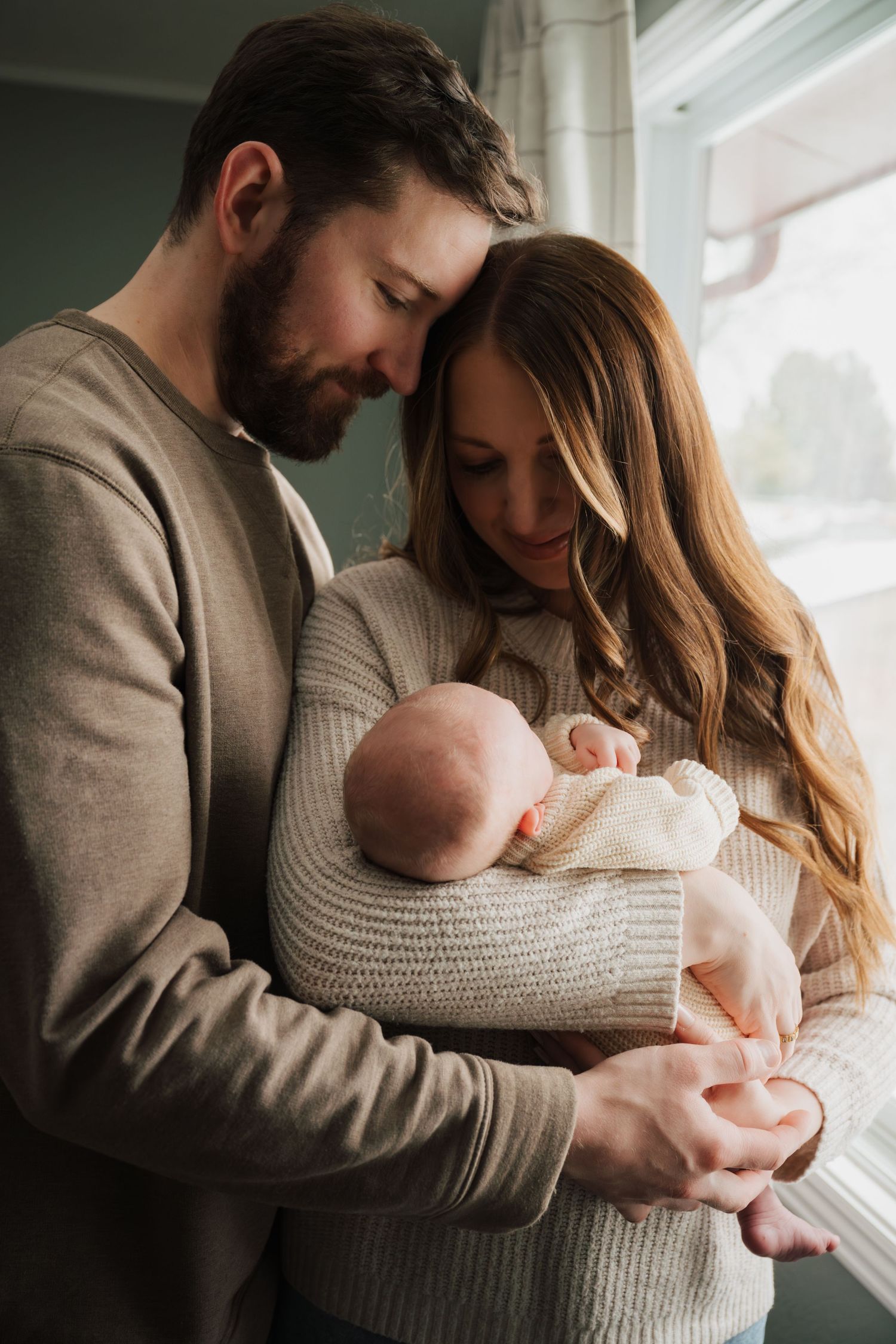 Tender family moment near a window with a newborn baby in knit clothing.