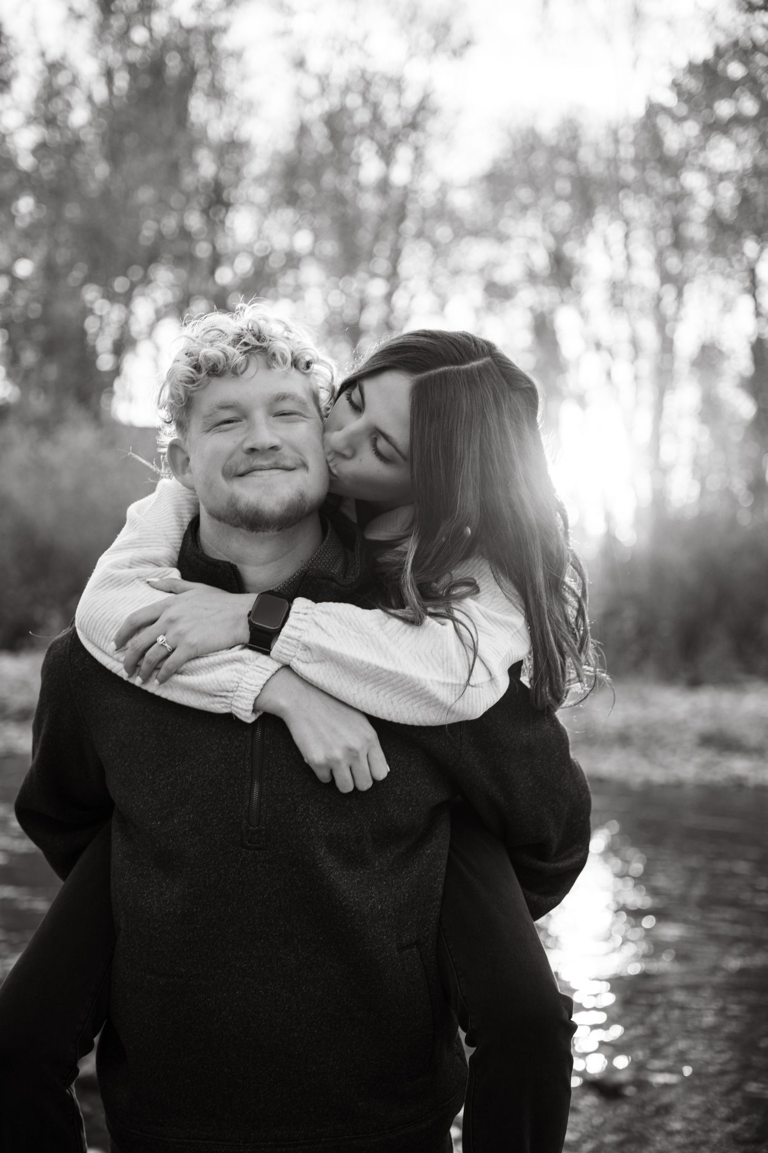 A joyful piggyback ride moment captured in black and white near a river.