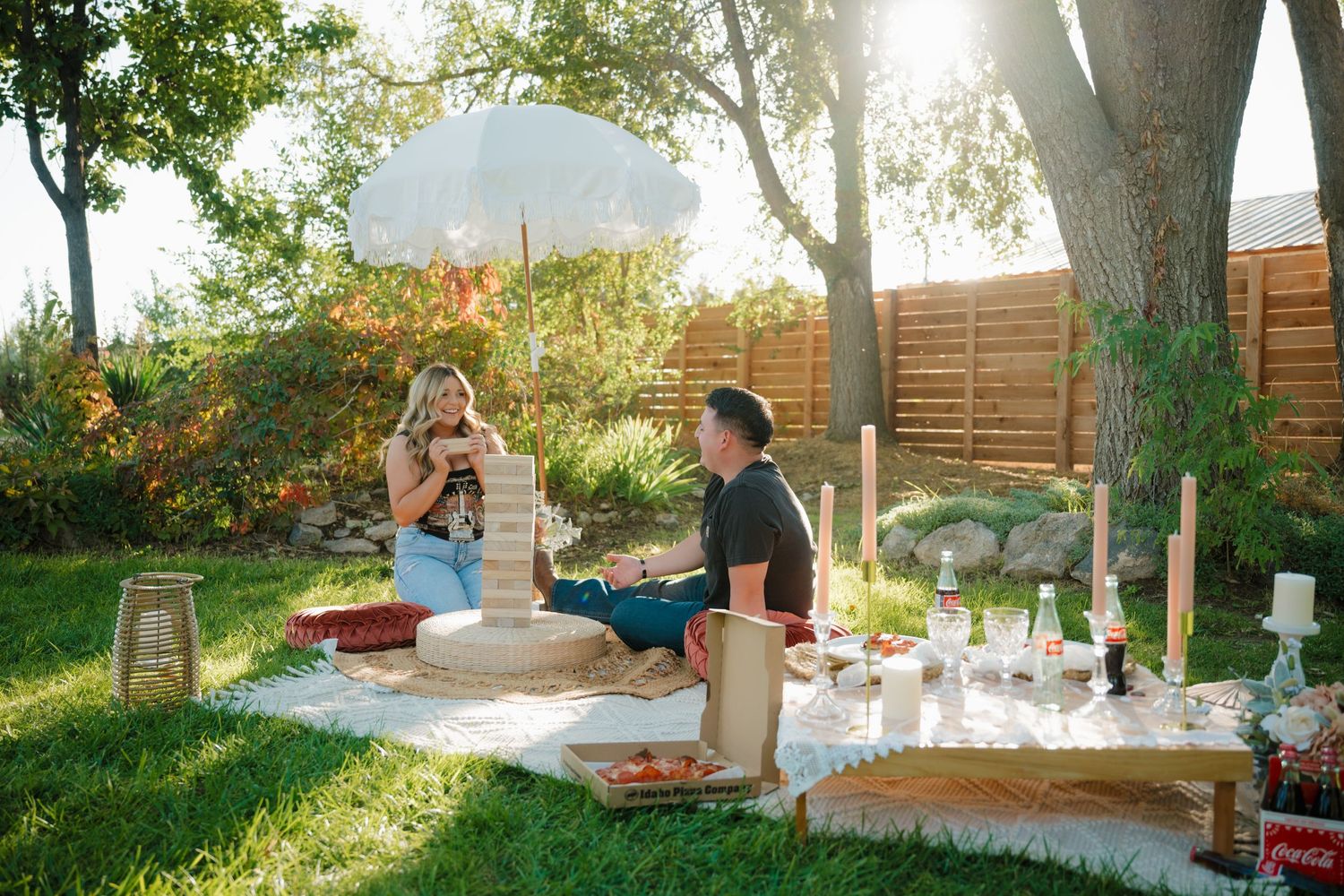 Couple enjoying a romantic picnic spread on blanket with decorative elements in a sunlit garden.