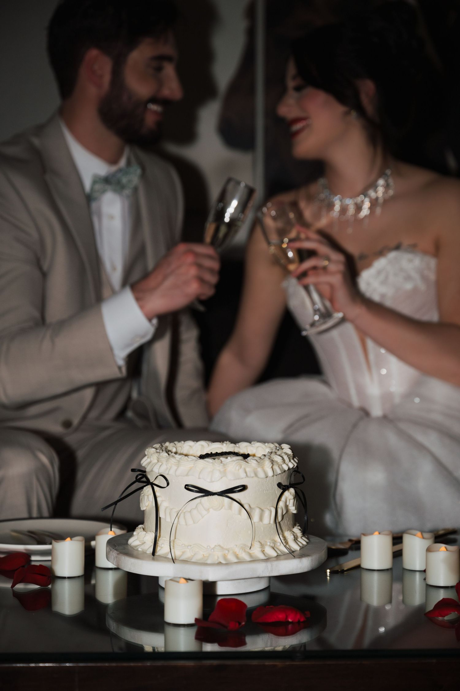Elegant wedding reception scene with white cake and champagne glasses in moody lighting.