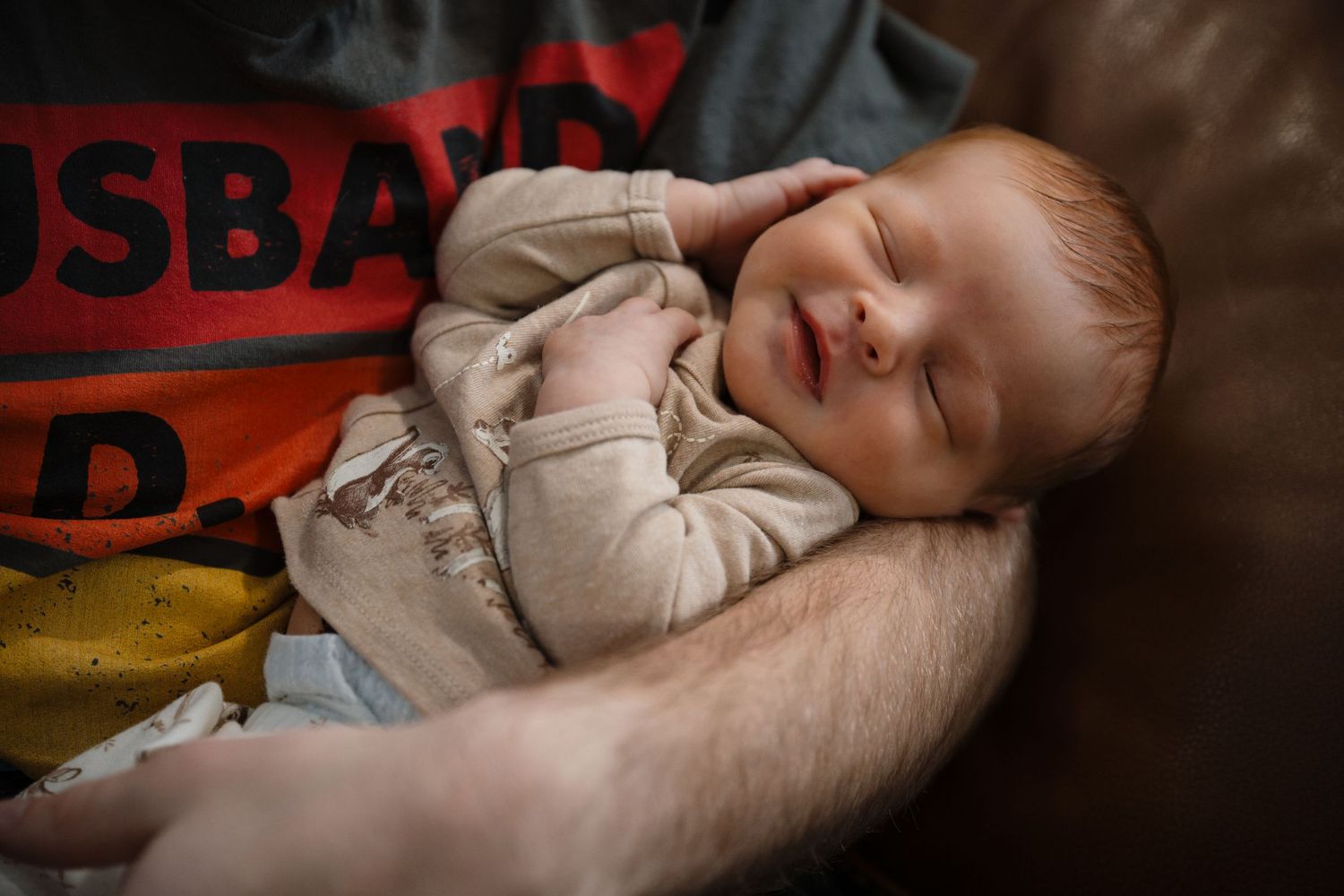 Peaceful sleeping infant in light colored clothing resting against a blanket.