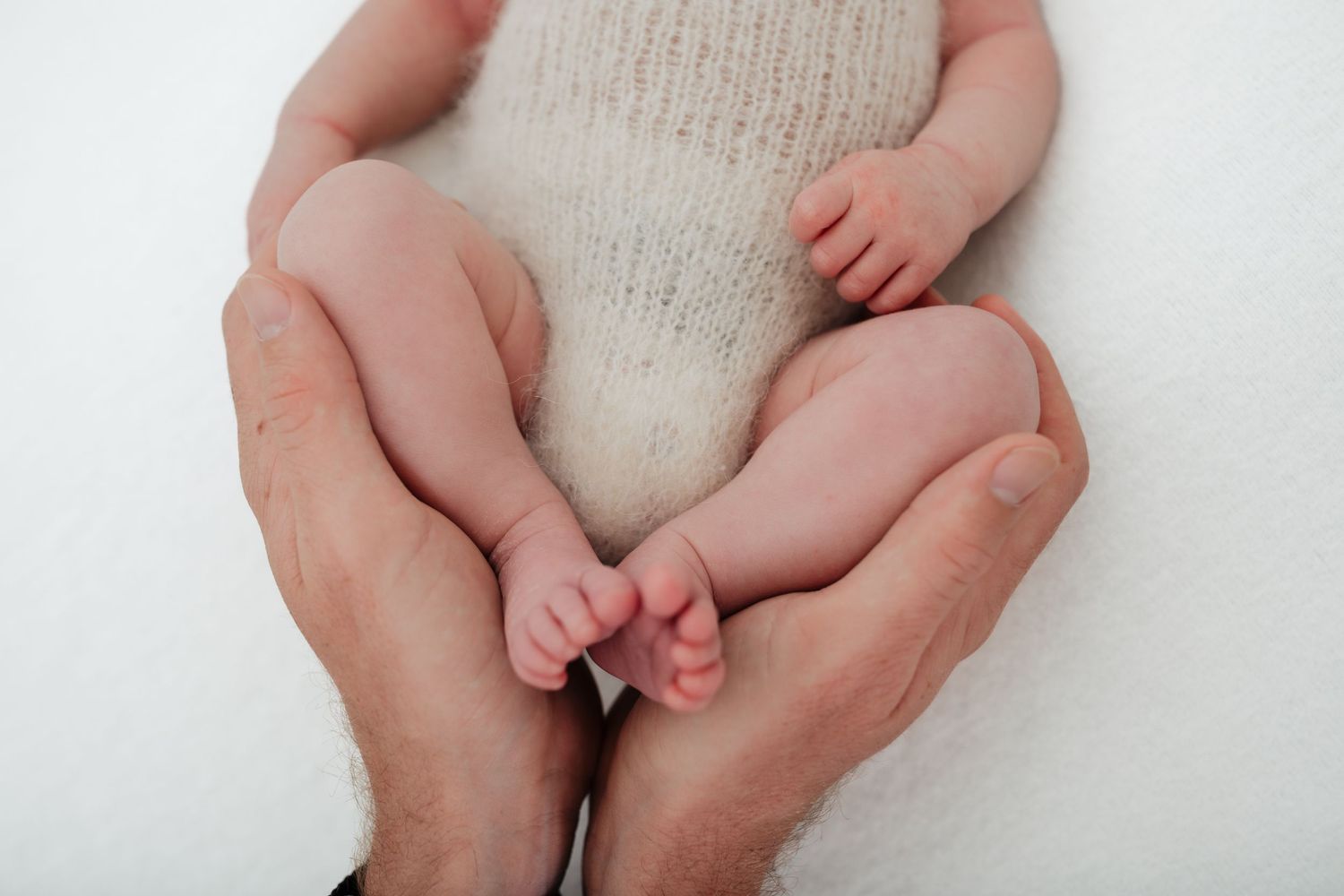 Close-up of baby's feet and legs against white knit fabric with hands supporting.
