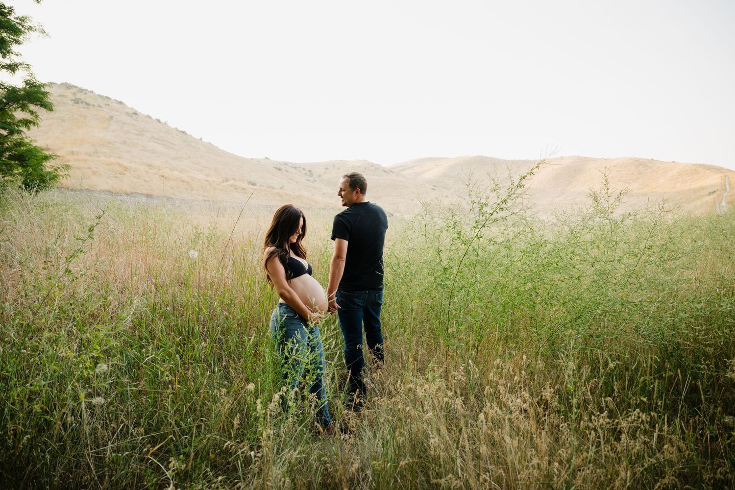 Two figures stand in a golden meadow against rolling hills on a misty afternoon.
