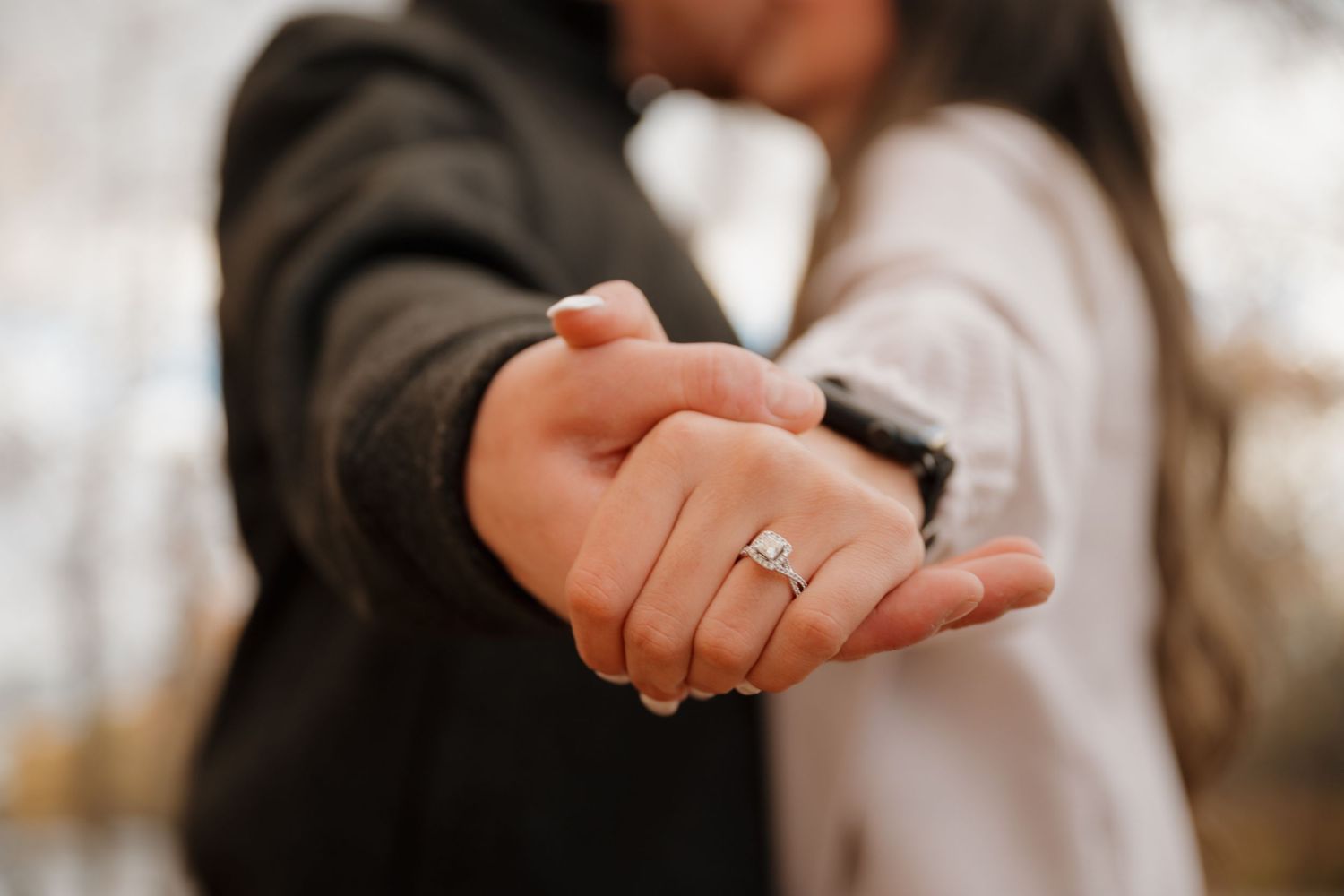 Close-up shot of joined hands with an engagement ring sparkling in soft focus.