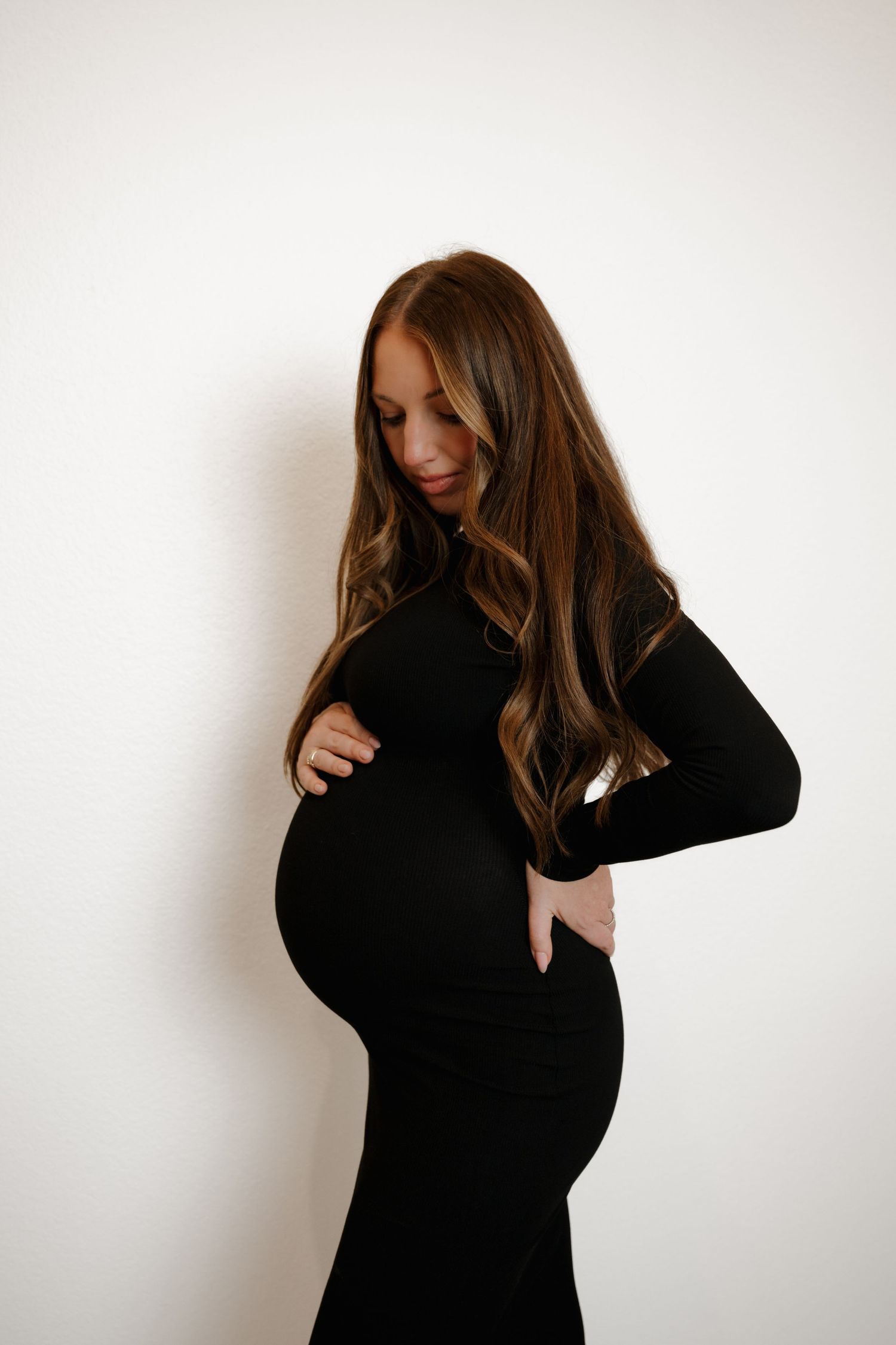 Side profile of expectant mother in black dress against white background.