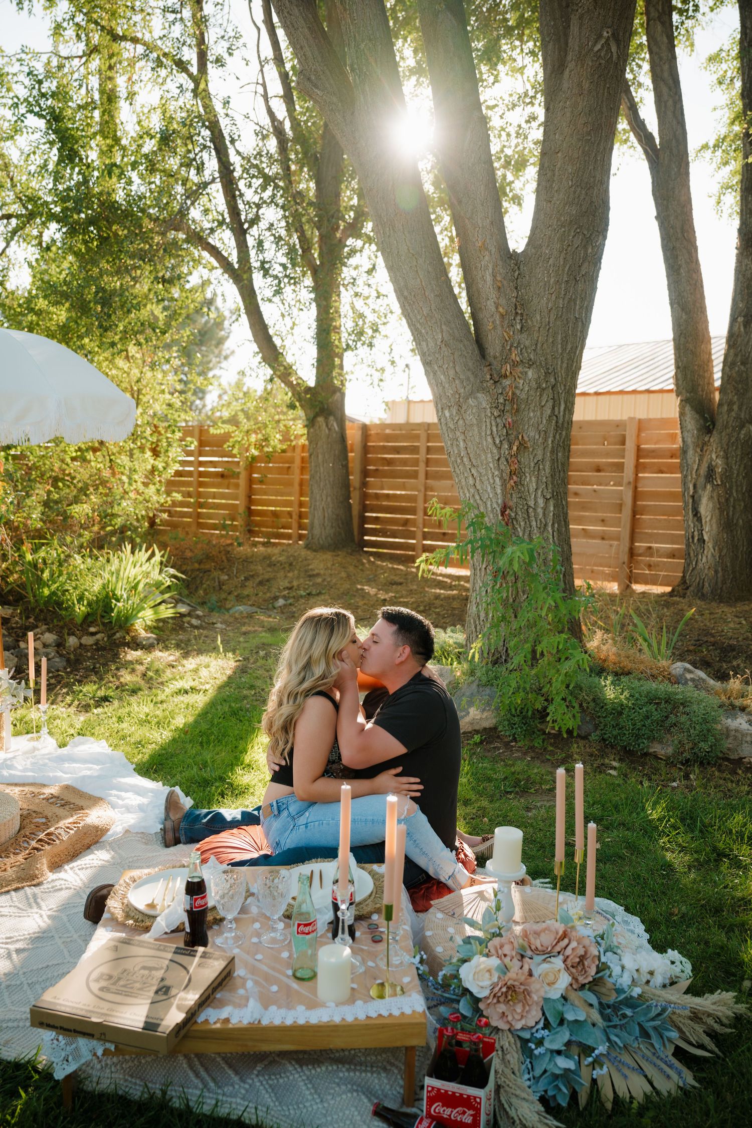 Romantic picnic setup under trees with blanket and decorations at sunset.