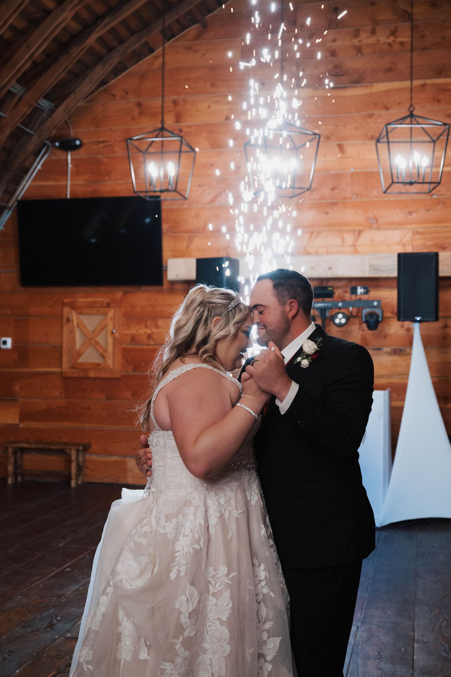 A romantic first dance moment in a rustic wooden barn venue with twinkling lights and lanterns overhead.