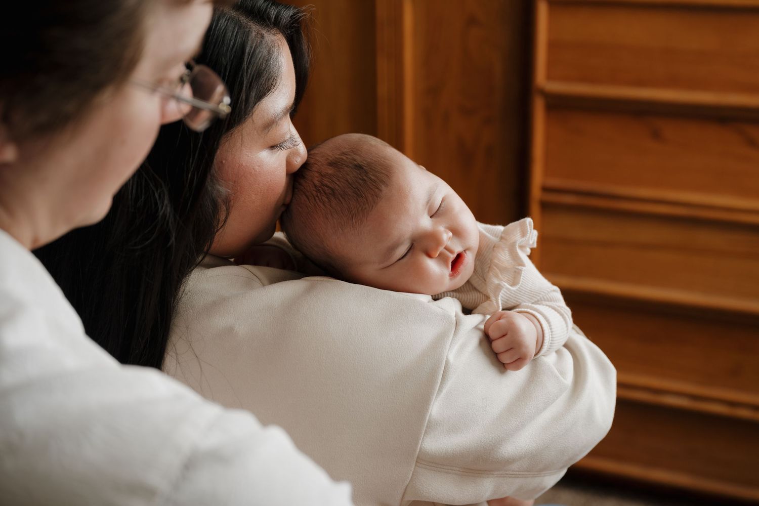 Intimate family moment as parents cradle their sleeping newborn against a wooden backdrop.