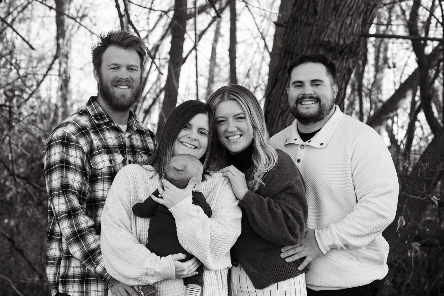 A group poses together in black and white wearing coordinated winter outfits in a wooded setting.
