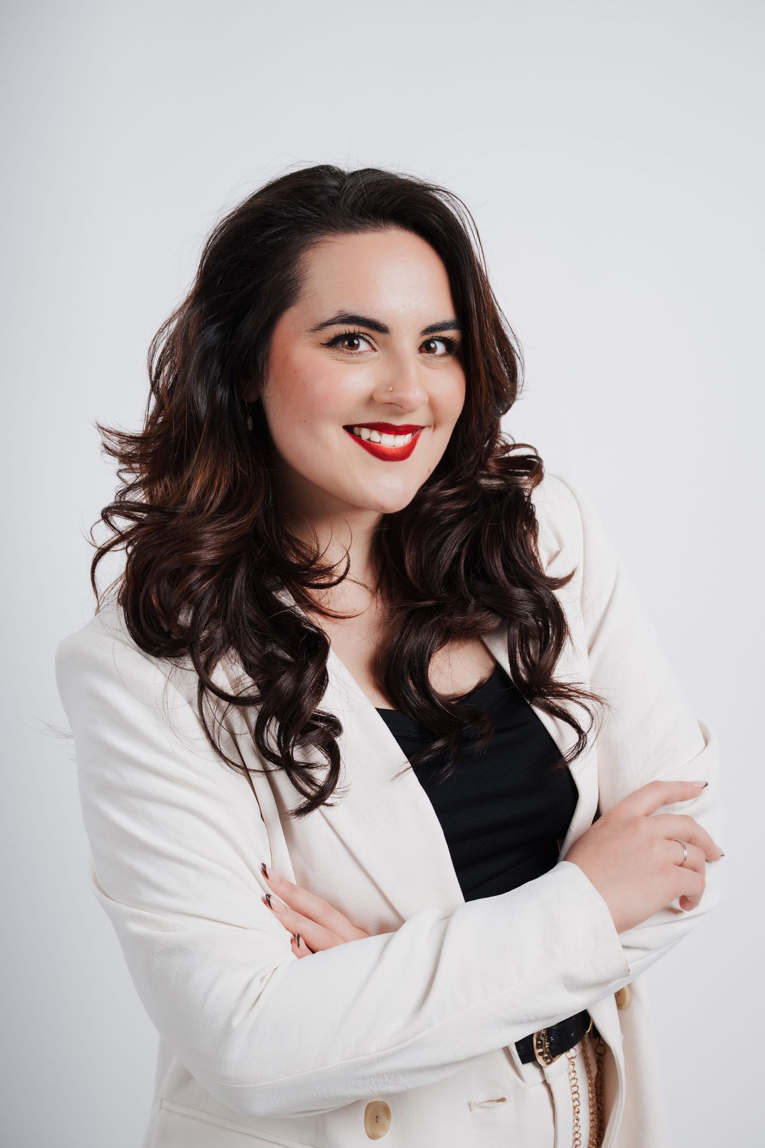 Professional portrait against white background showing confident pose in white blazer with bold red lipstick and dark wavy hair.
