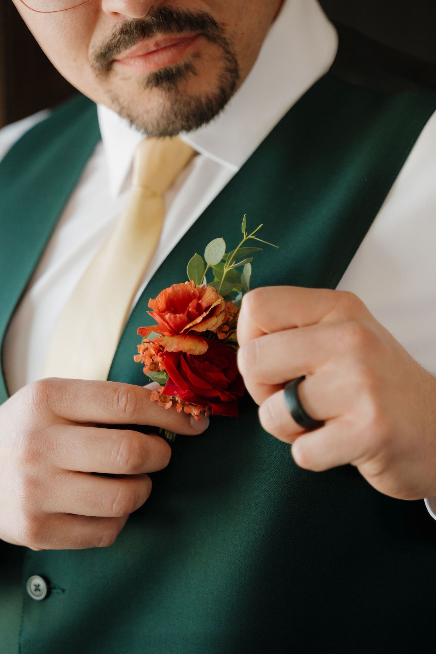Close-up of hands pinning a red rose boutonniere on an emerald green vest.