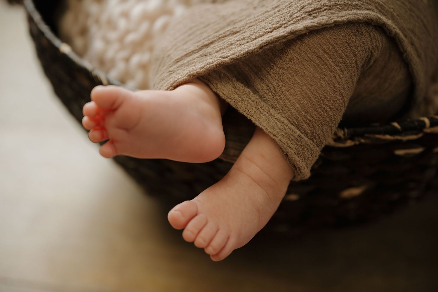 Tiny baby feet peek out from beneath a brown textured blanket.