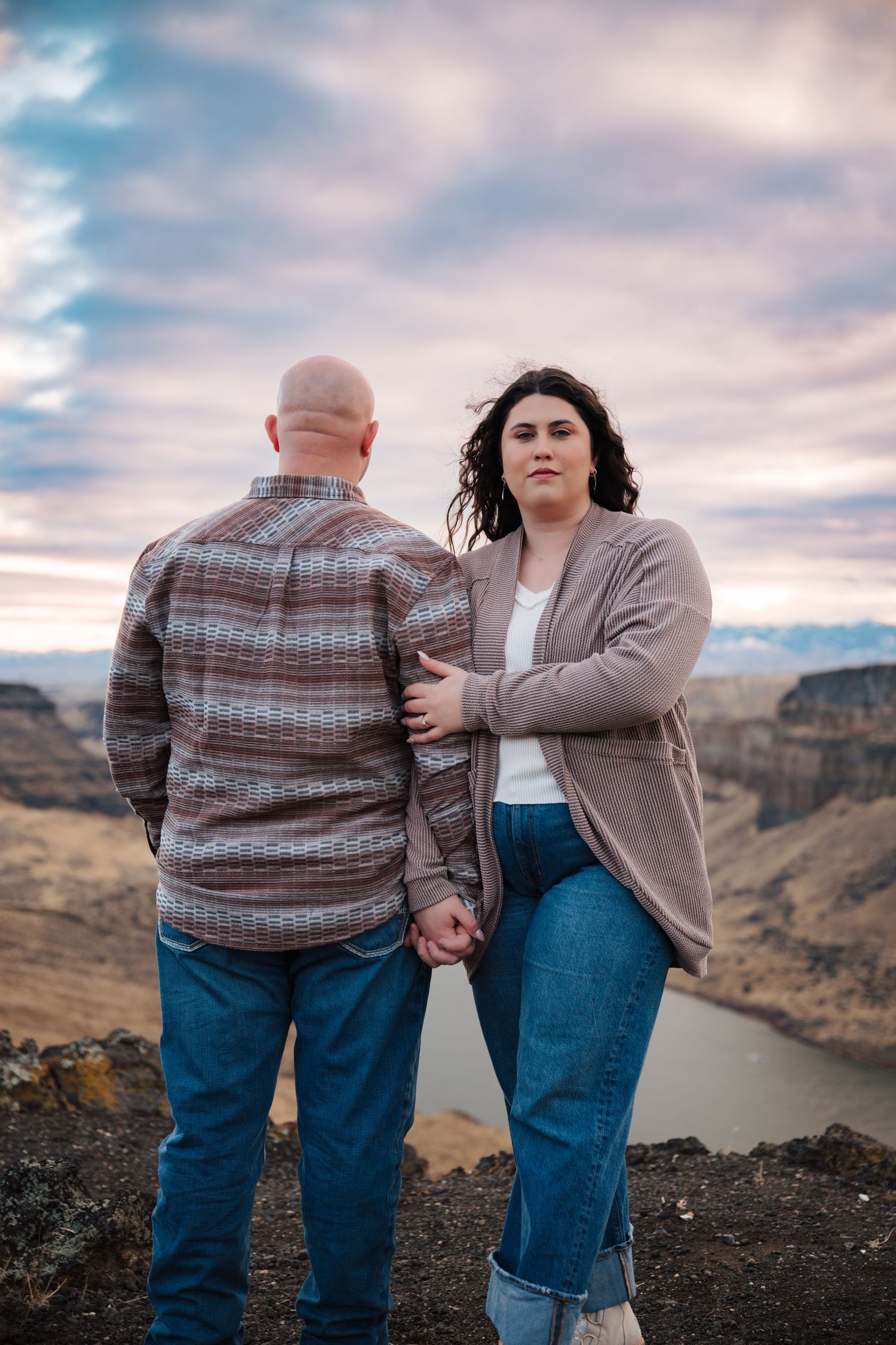 A couple shares a tender moment while standing on a rocky overlook with a winding river below.