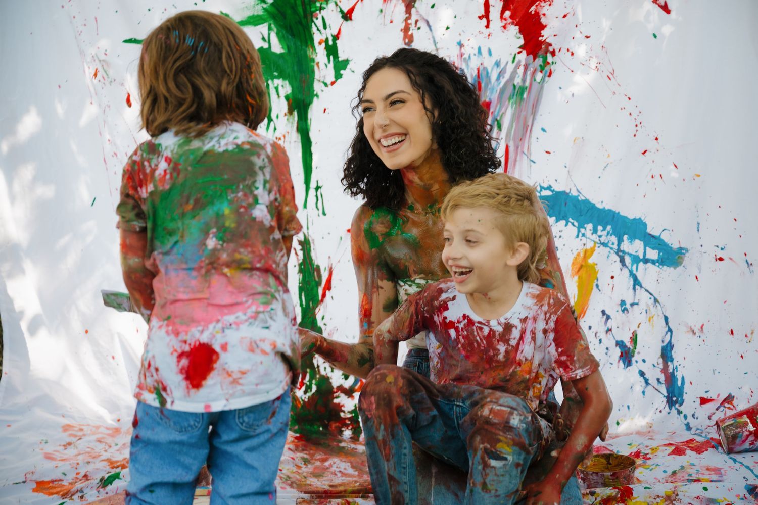 Joyful paint splatter art session with children and adult creating colorful mess outdoors.