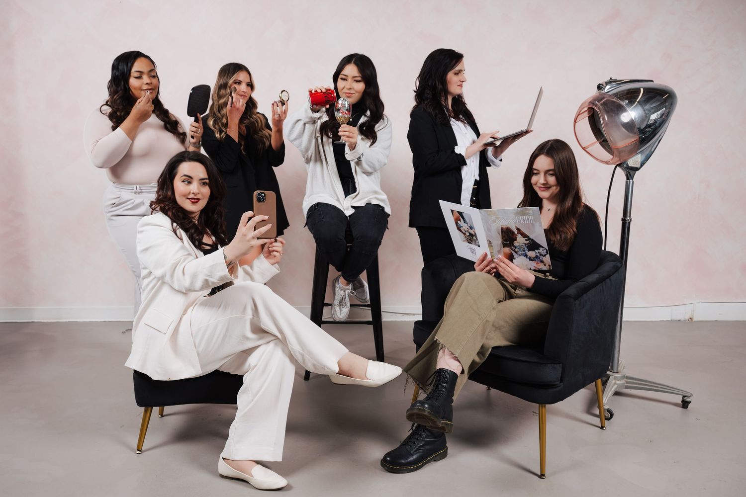 Group of people posing with mobile phones and silver heart balloon in studio with light backdrop.