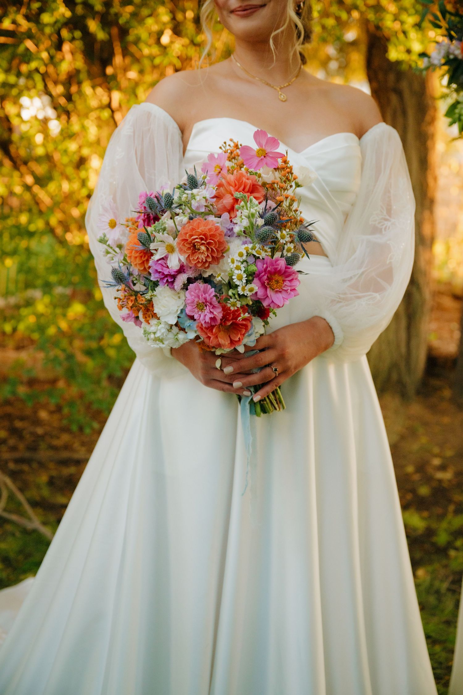 A colorful bridal bouquet with coral and pink flowers against a white wedding dress.