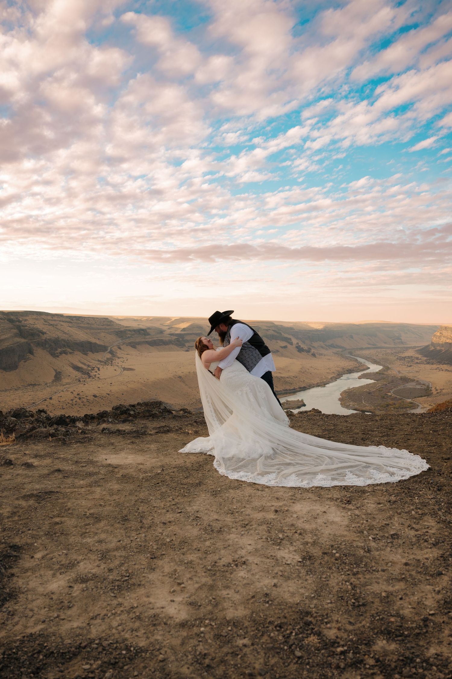 Epic wedding photo of couple kissing on cliff edge overlooking winding river canyon.