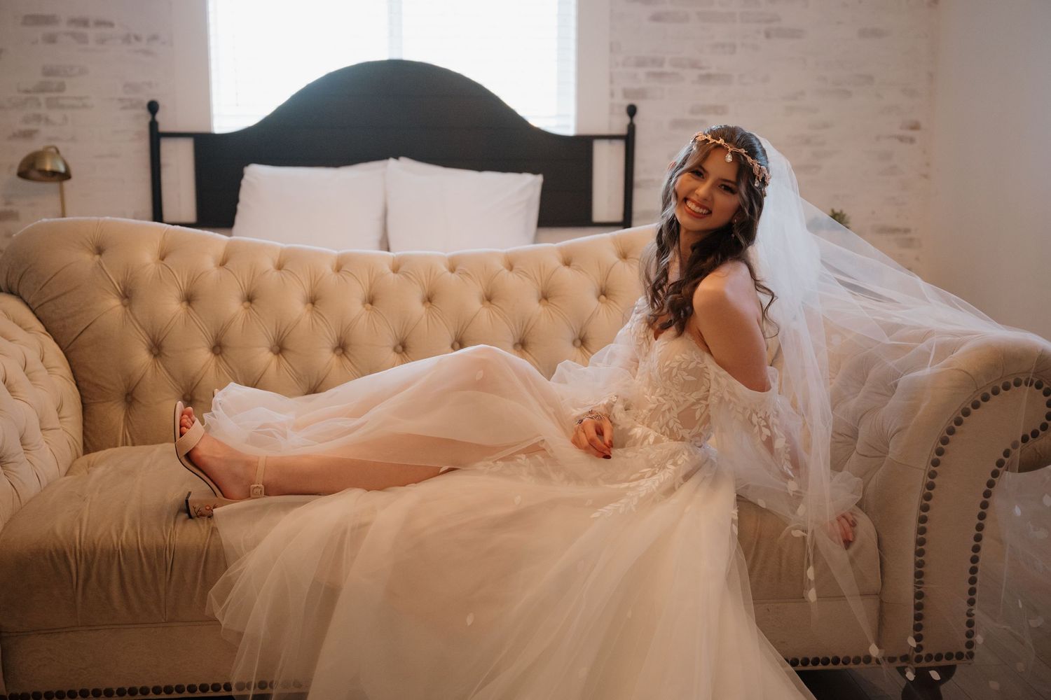 A bride in a flowing white dress reclines on a beige tufted sofa.