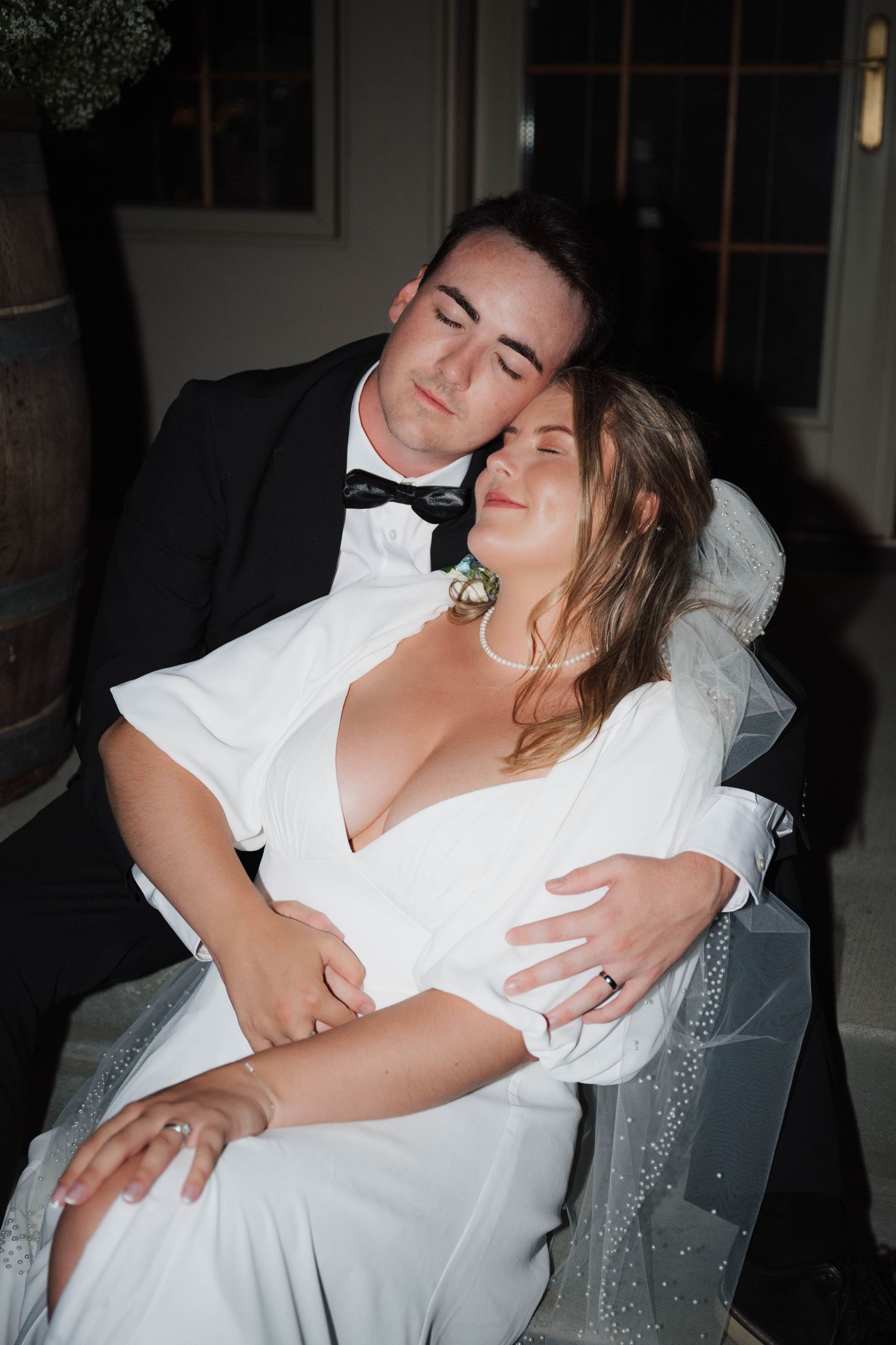 A romantic wedding moment captured as newlyweds share an intimate embrace while seated together in low light.