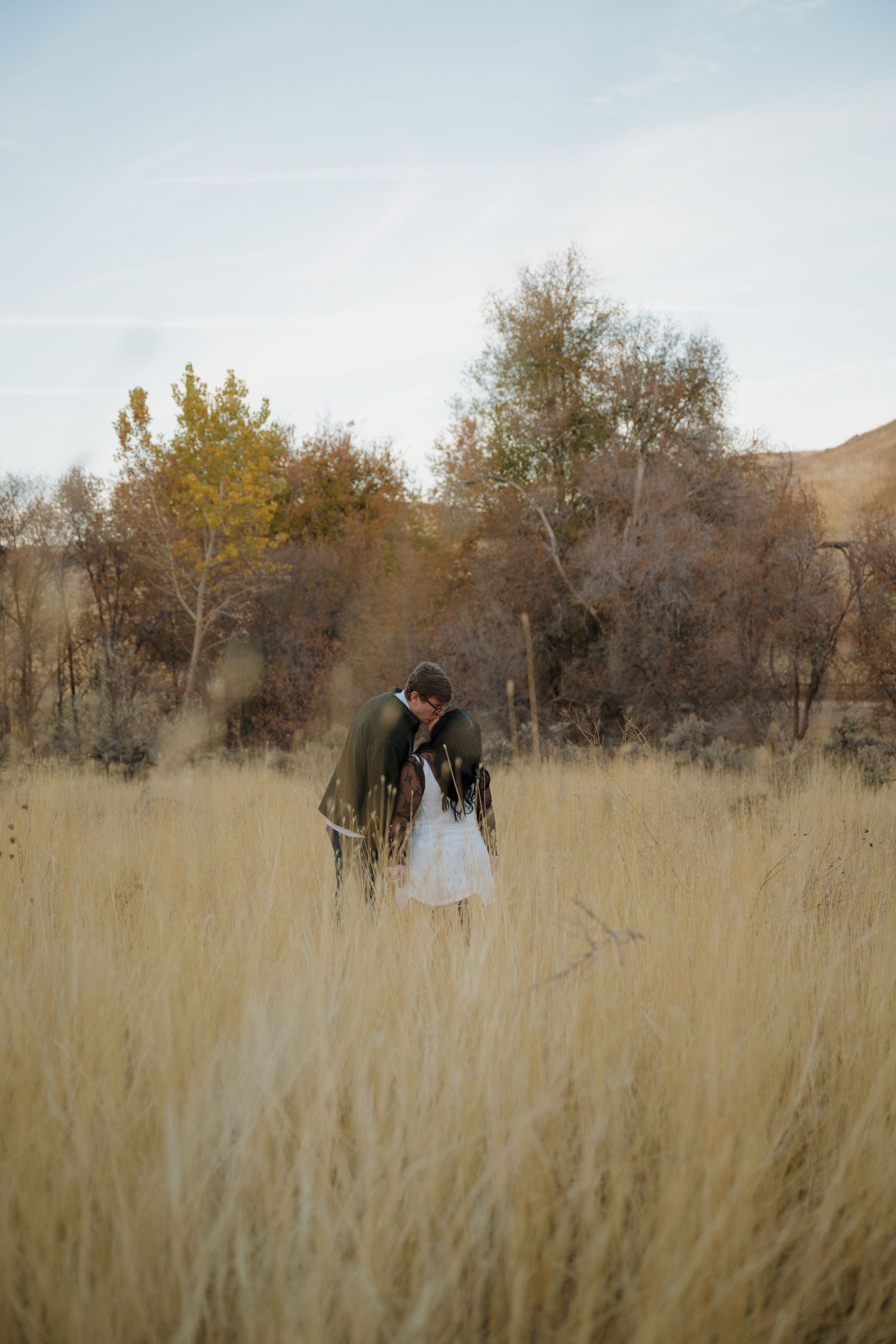 Two figures share an intimate moment amid tall wheat fields during golden hour.