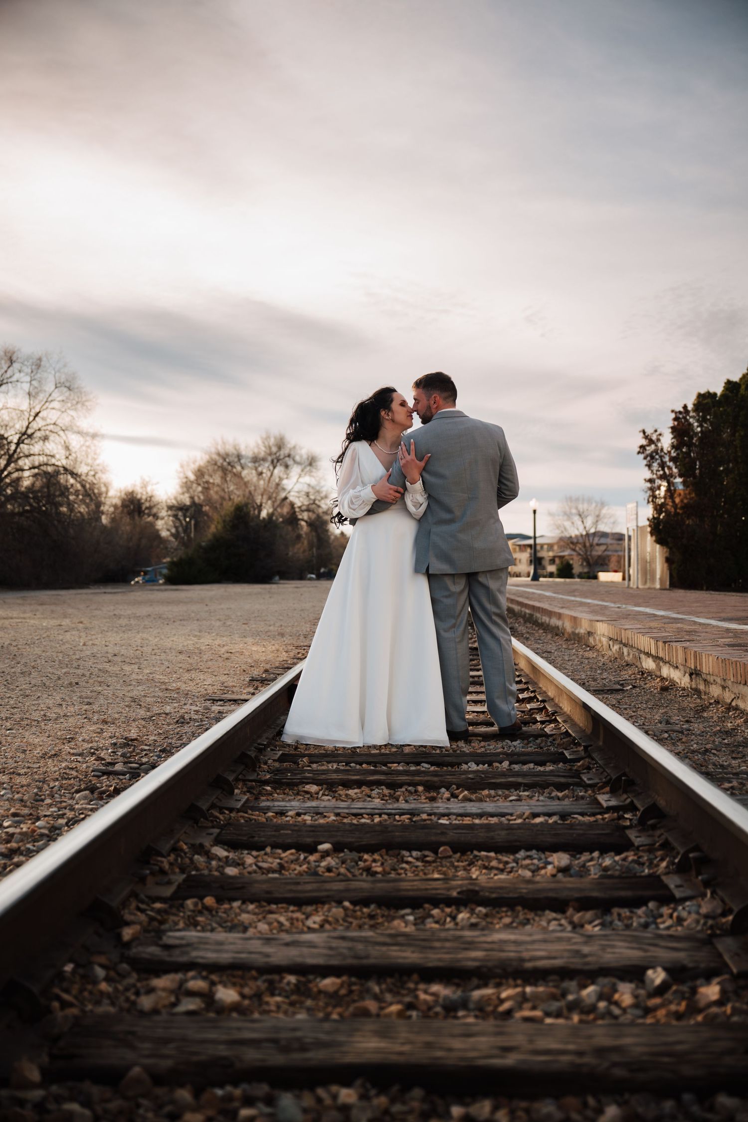 Romantic wedding photo of couple standing on train tracks at sunset.