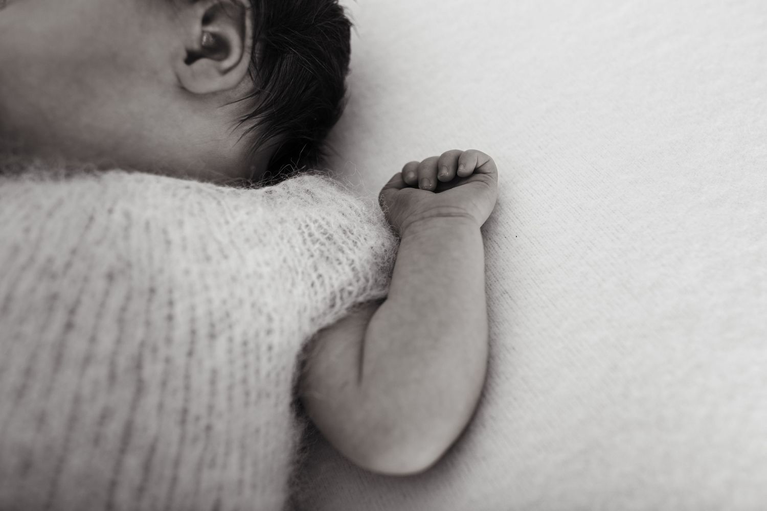 Close-up black and white photo of a sleeping baby's arm and shoulder in a white sweater.