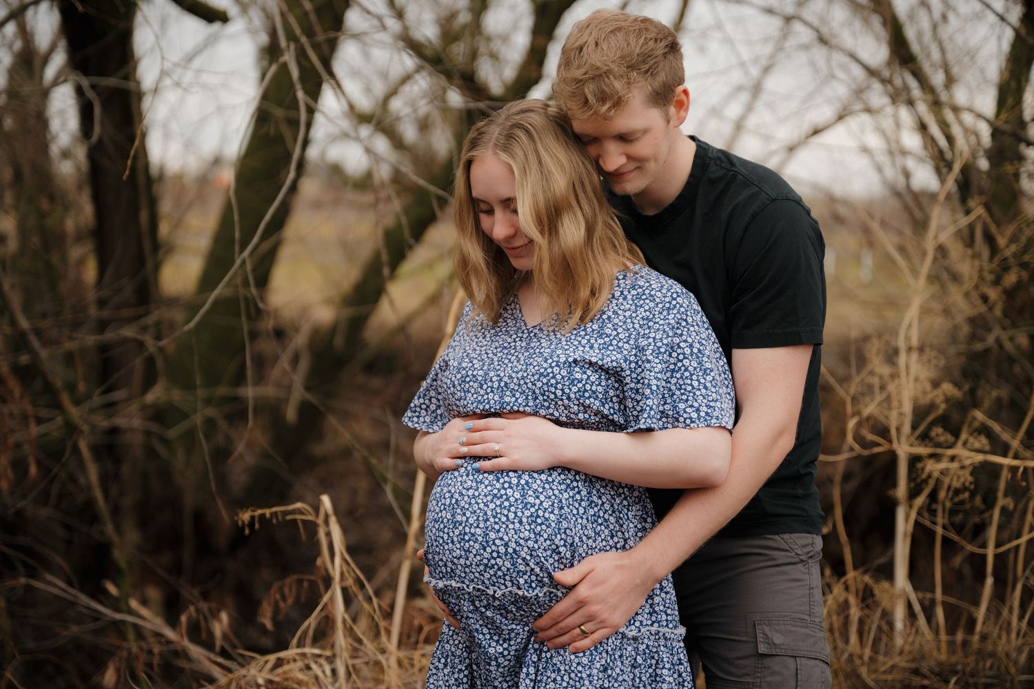 Couple sharing an intimate moment during outdoor maternity photoshoot in natural setting.