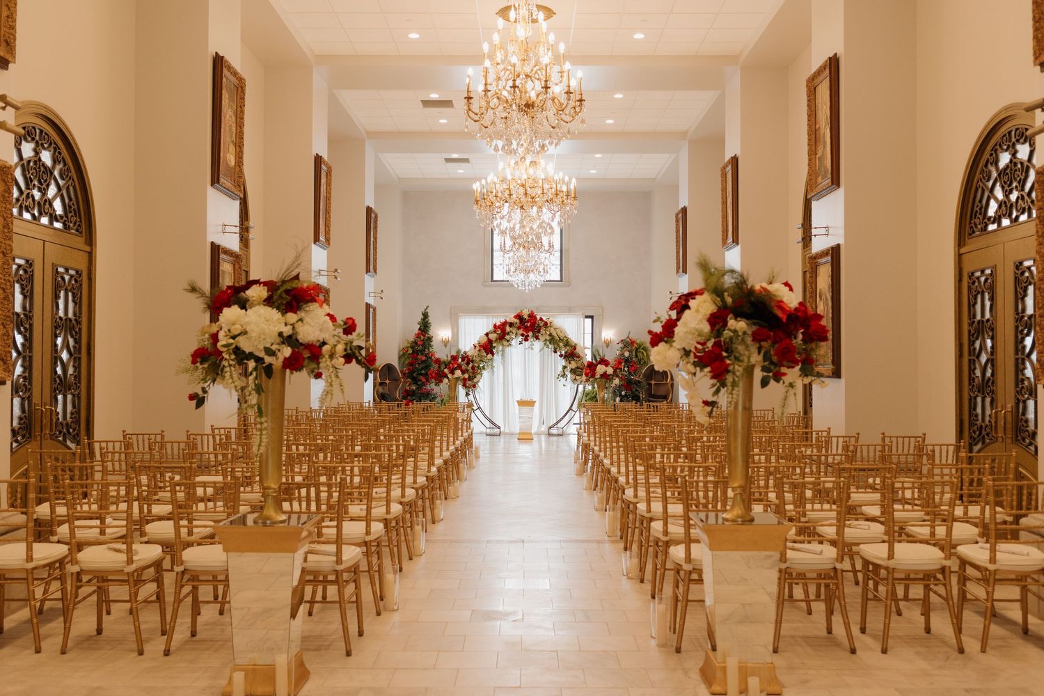 Elegant wedding ceremony venue with gold chairs, crystal chandeliers, and pink floral arrangements lining the aisle.