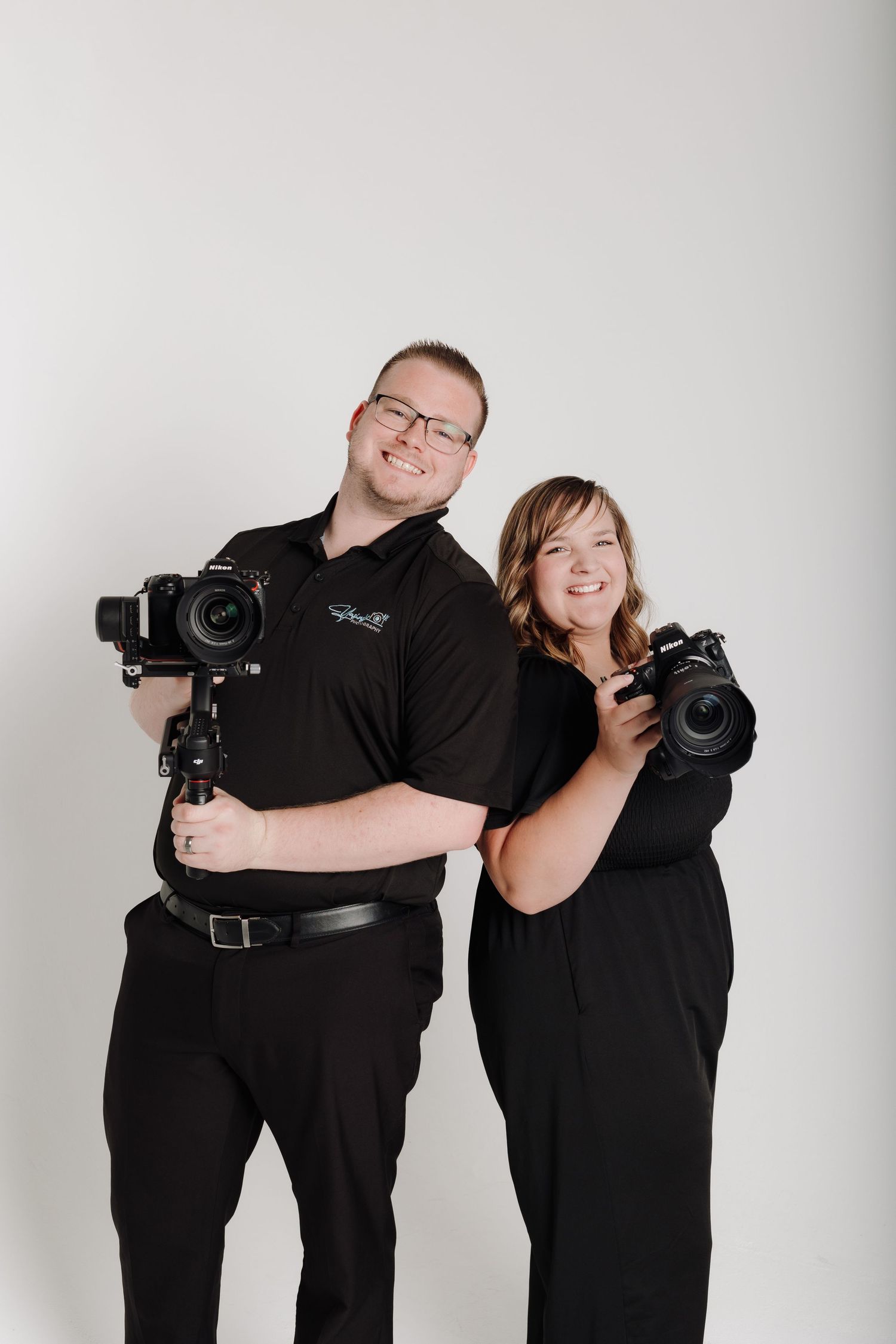 Photography team in matching black outfits pose with professional cameras against white background.