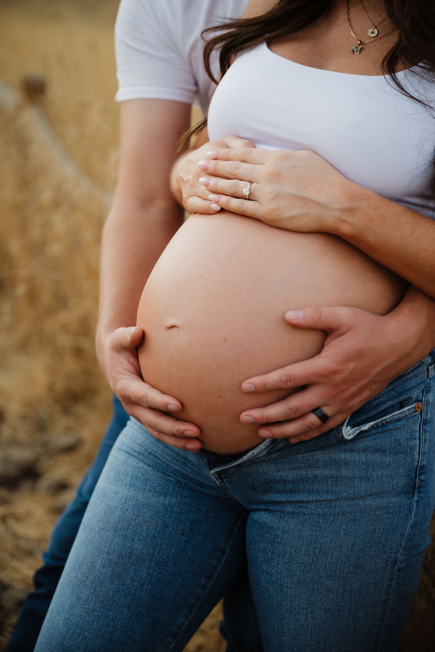 Close-up shot of hands cradling a pregnant belly while wearing blue jeans and a white shirt.