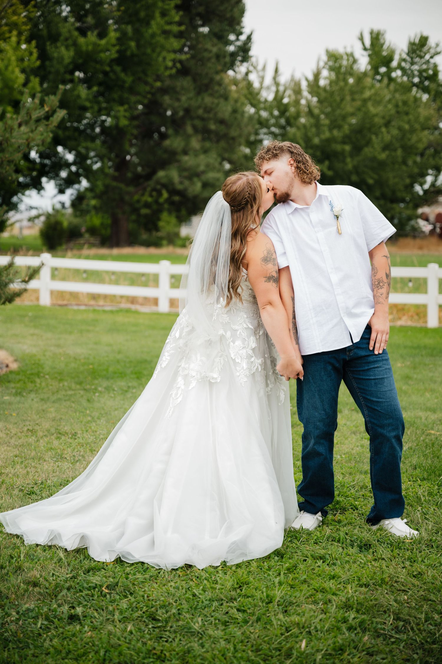 A romantic wedding photo of a couple sharing an intimate moment on a rustic farm with white fences.