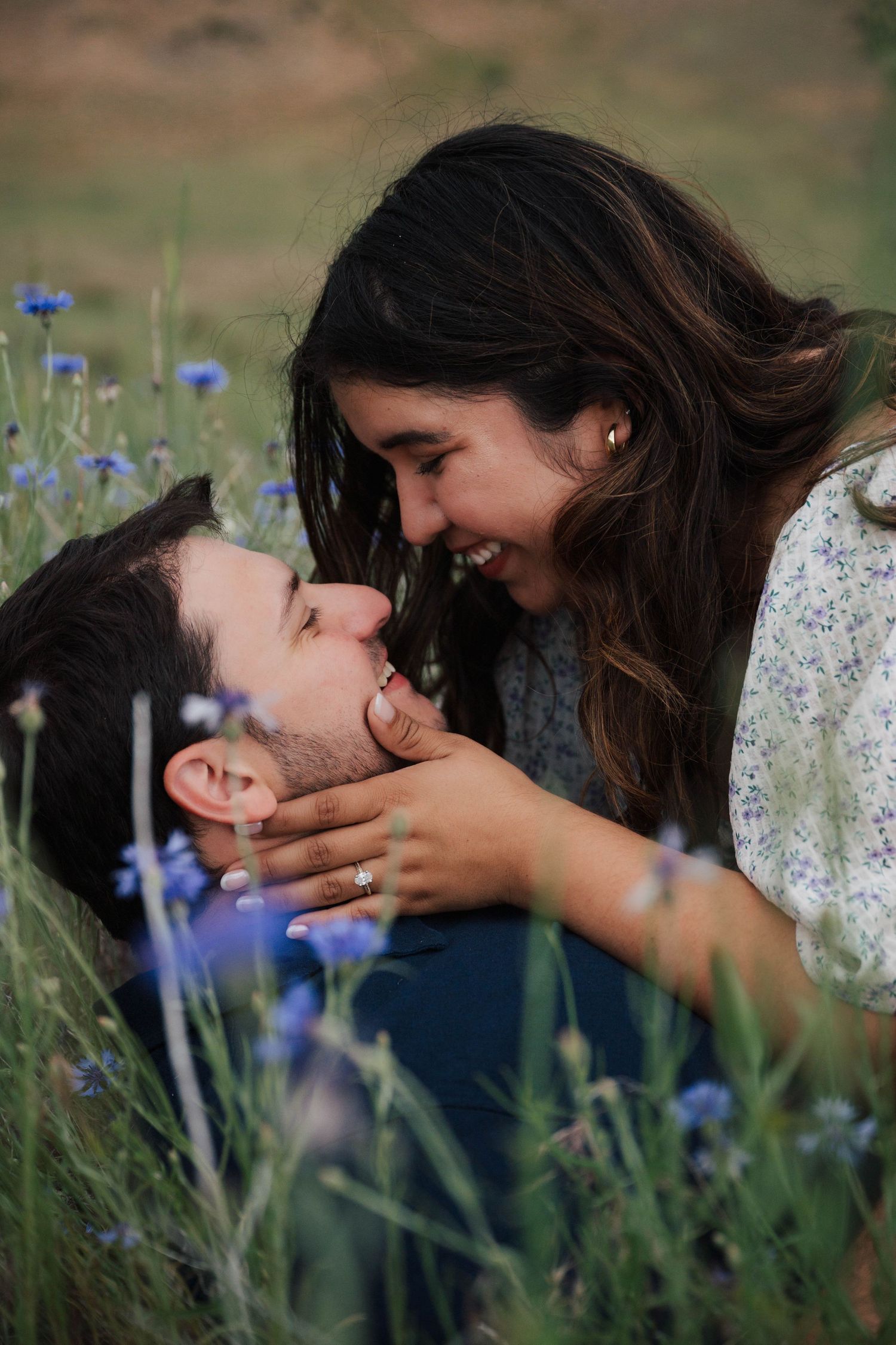 A romantic couple shares a joyful moment while lying in a field of purple wildflowers on a sunny afternoon.