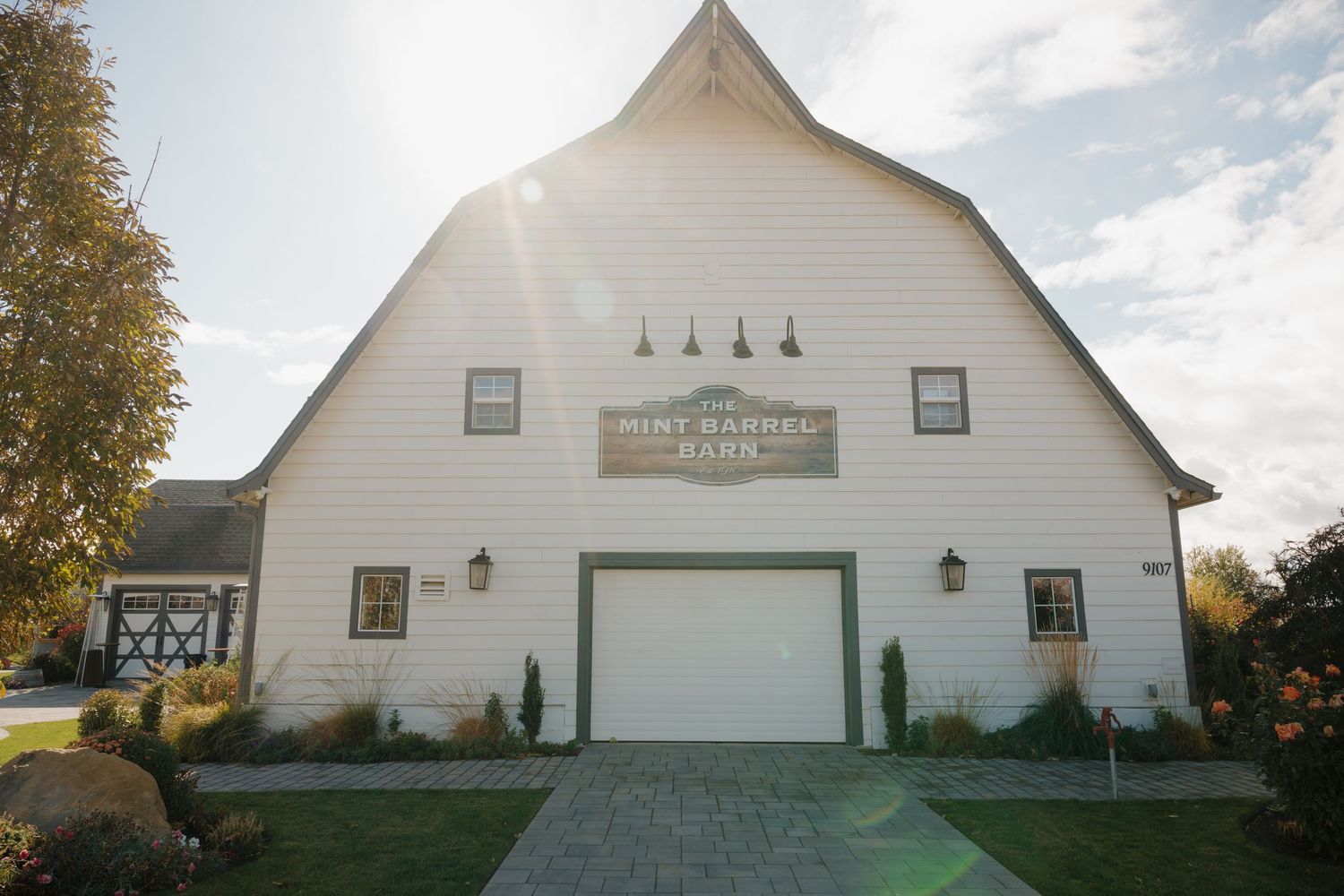 A white barn-style wedding venue with a peaked roof and large garage door entrance photographed at sunset.