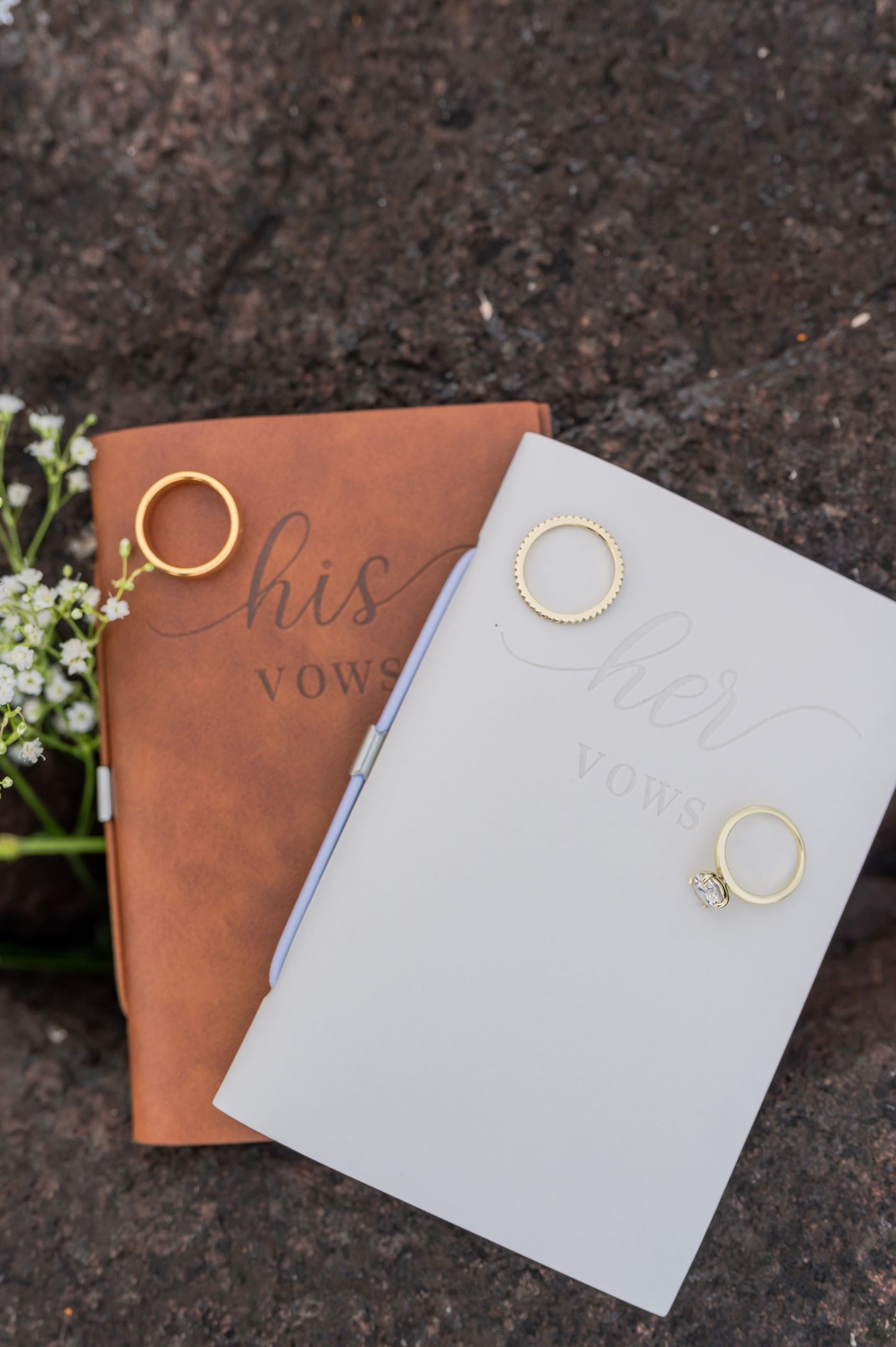 His and her wedding vow books in brown and white leather with wedding rings placed on top.